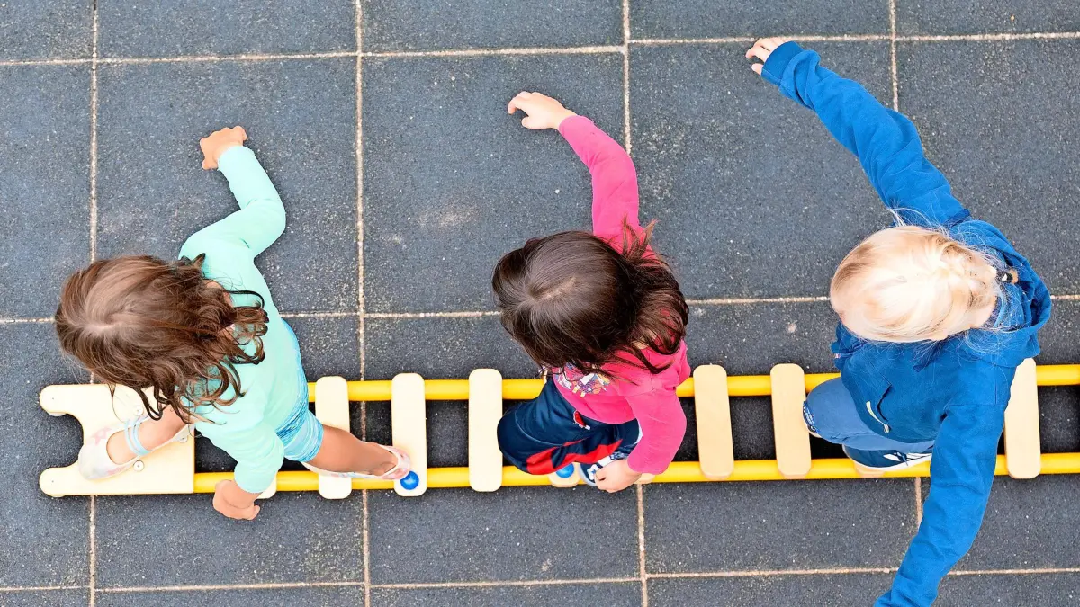 Kinder balancieren während eines Pressetermins auf dem Spielplatz einer Kindertagesstätte auf einem Brett. (zu dpa «Kitaleitungskongress mit Studie von VBE zu Personalmangel - weitere Kita-Erhebung von Bertelsmann Stiftung») +++ dpa-Bildfunk +++
