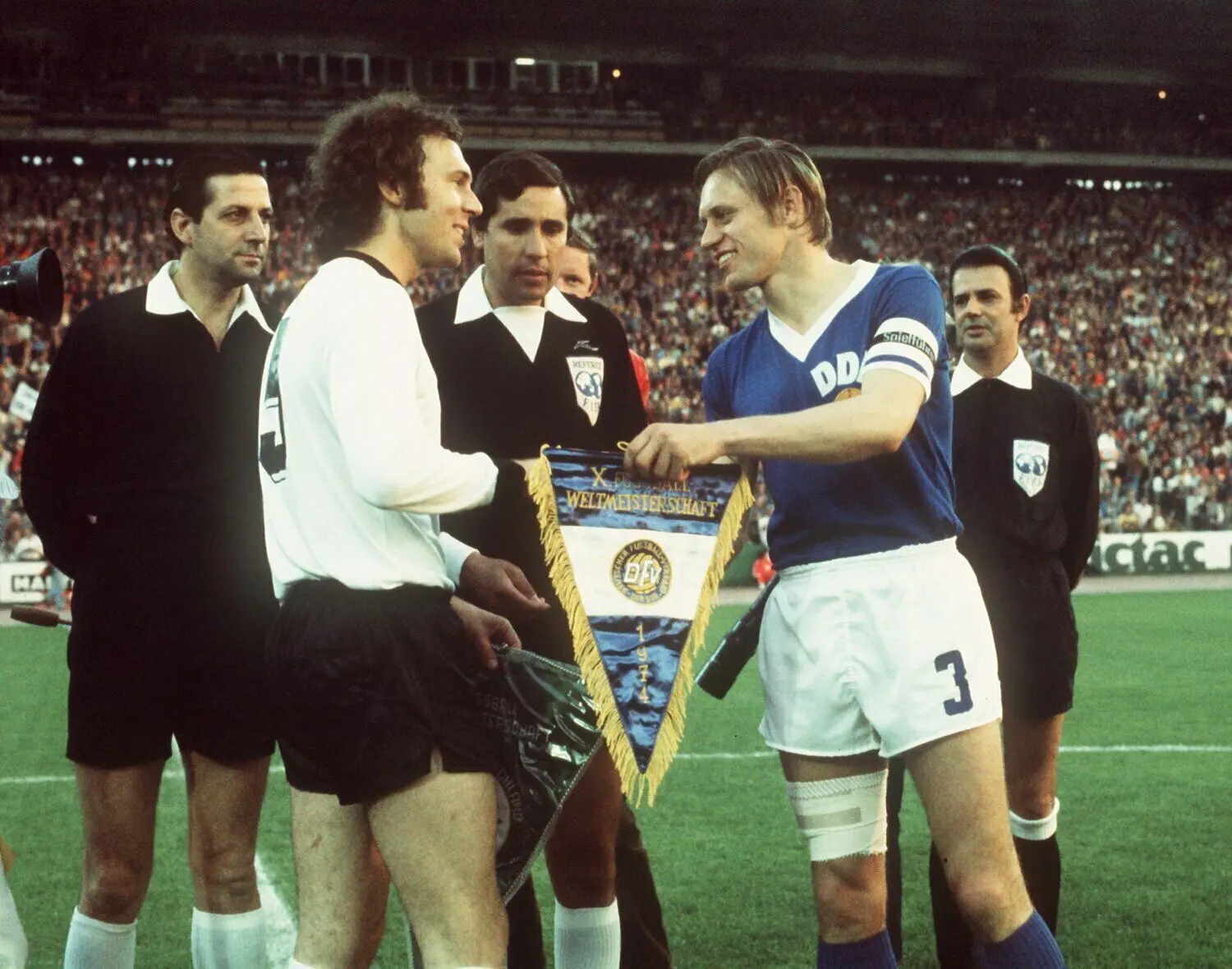 Wimpeltausch der Kapitäne Franz Beckenbauer (l.) und Bernd Bransch (r.) am 22.06.1974 im Hamburger Volksparkstadion. Der uruguayische Schiedsrichter Ramon Barretto Ruiz (M.) schaut mit seinen Linienrichtern zu. Die Fußballnationalmannschaft der Bundesrepublik verlor auf ihrem Weg zum Titelgewinn das Gruppenspiel der Fußball-WM gegen die DDR-Elf mit 0:1.