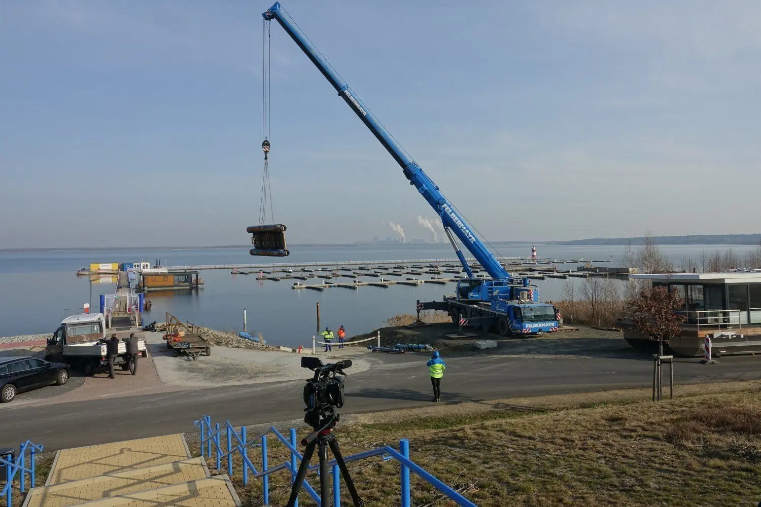 Bevor das schwimmende Haus, was am Ufer wartet, eingehoben werden kann, schwebt die Arbeitsplattform ein. Mit der wird das Haus dann an seinen Liegeplatz geschoben.