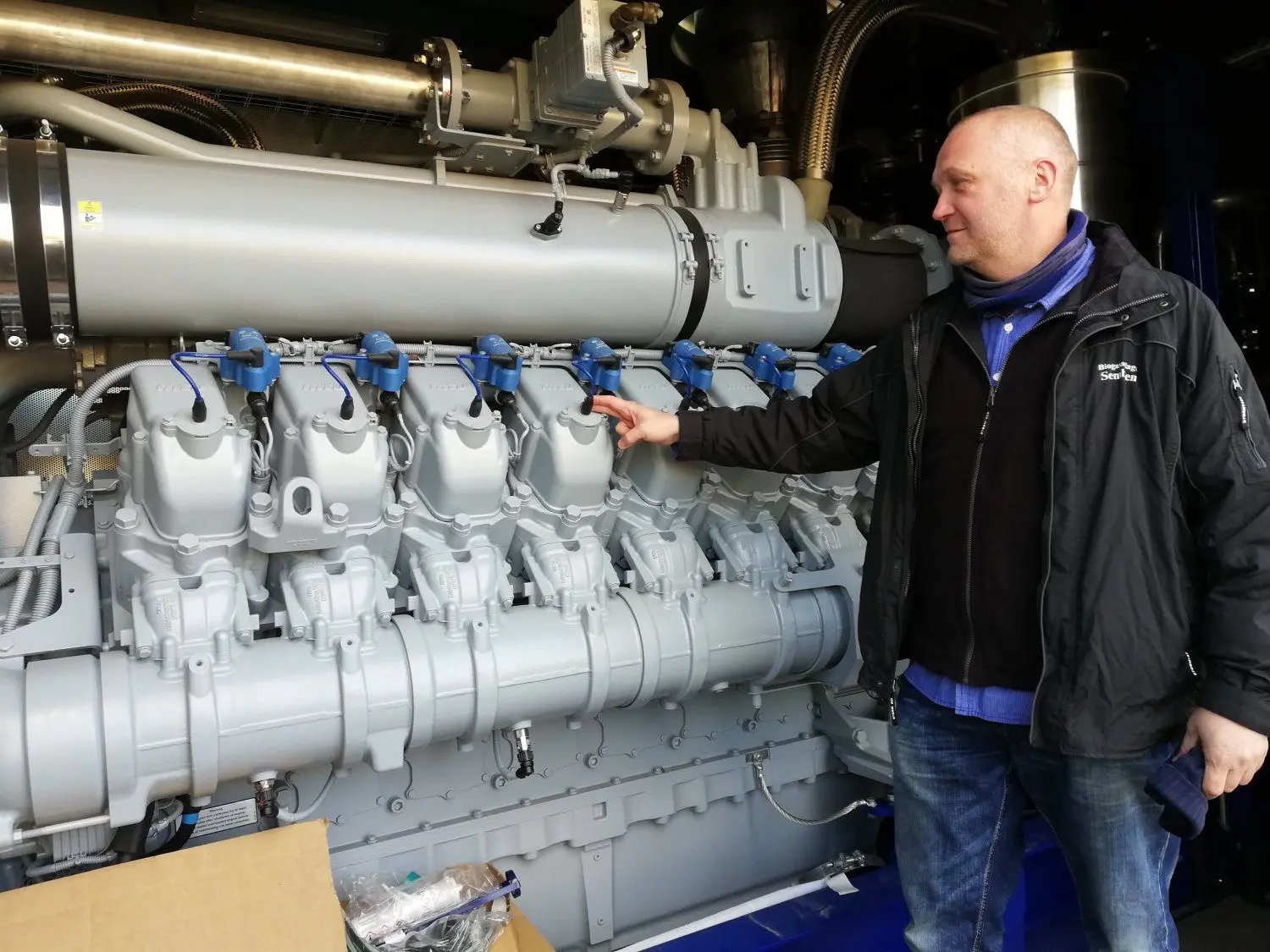 Frank Häsler zeigt das Herzstück eines der neuen Blockheizkraftwerke der Anlage. Das Biogas aus dem Fermenter ist der Treibstoff für diese Verbrennungsmaschine. Ihre Aufgabe ist es, einen Generator zur Stromerzeugung anzutreiben. Der so erzeugte Strom wird in Sembten ins Verteilnetz des regionalen Netzbetreibers Mitnetz Strom eingespeist.