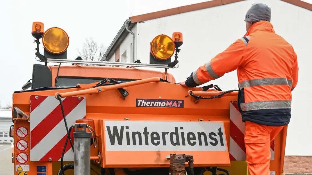 Ein Mitarbeiter vom Landesbetrieb Straßenwesen steht auf einem Streufahrzeug und überprüft die Ladung Streusalz.