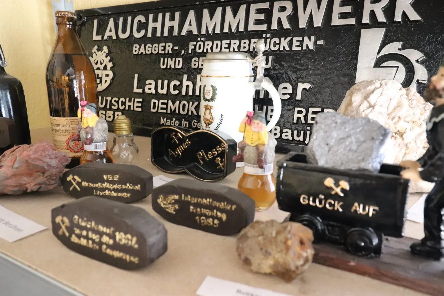 Ein Firmenschild aus dem Lauchhammerwerk, Zierbriketts und eine Flasche Bergmannsschnaps, genannt „Kumpeltod“.