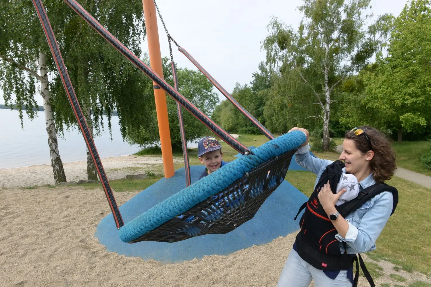 Sarah Dombrowe hat Spaß mit ihren Kindern auf dem Spielplatz am Senftenberger Stadthafen. Der vierjährige Luca in der Korbschaukel und der neugeborene Lian schläft an Mamas Körper.