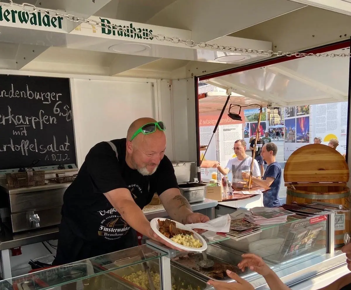 Finsterwaldes Brauhaus-Küchenchef Frank Bansner reicht in Halle Bierkarpfen über den Imbiswagen-Tresen.