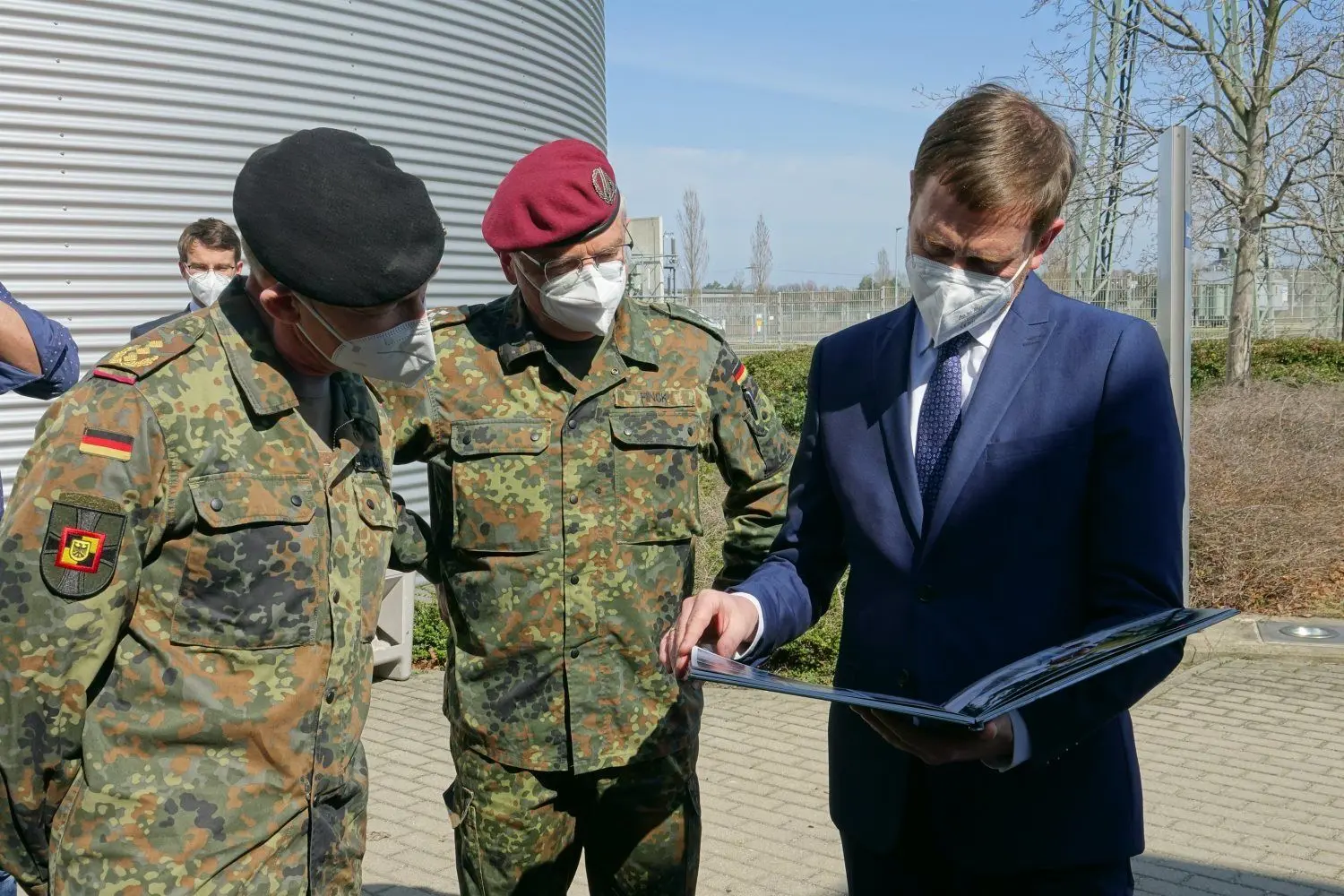 Oberst Klaus Finck, Generalleutnant Kai Rohrschneider und Ministerpräsident Michael Kretschmer (v.l.n.r.) schauen ein Buch an, was den Hilfseinsatz der Bundesweh bei der Bekämpfung der Corona-Pandemie dokumentiert. Derzeit läuft wieder ein Einsatz im Kreis Görlitz.