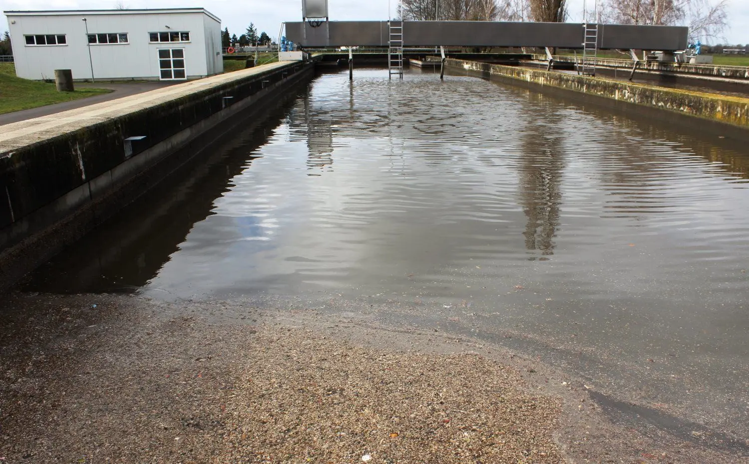 Das Ab- und Regenwasser wird nach der Entfernung groben Unrates in Rückhaltebecken gepumpt. Im Hintergrund ist die Räumerbrücke zu sehen, die die  anfallenden absetzbaren Stoffe zum Rechenraum zurück führt.