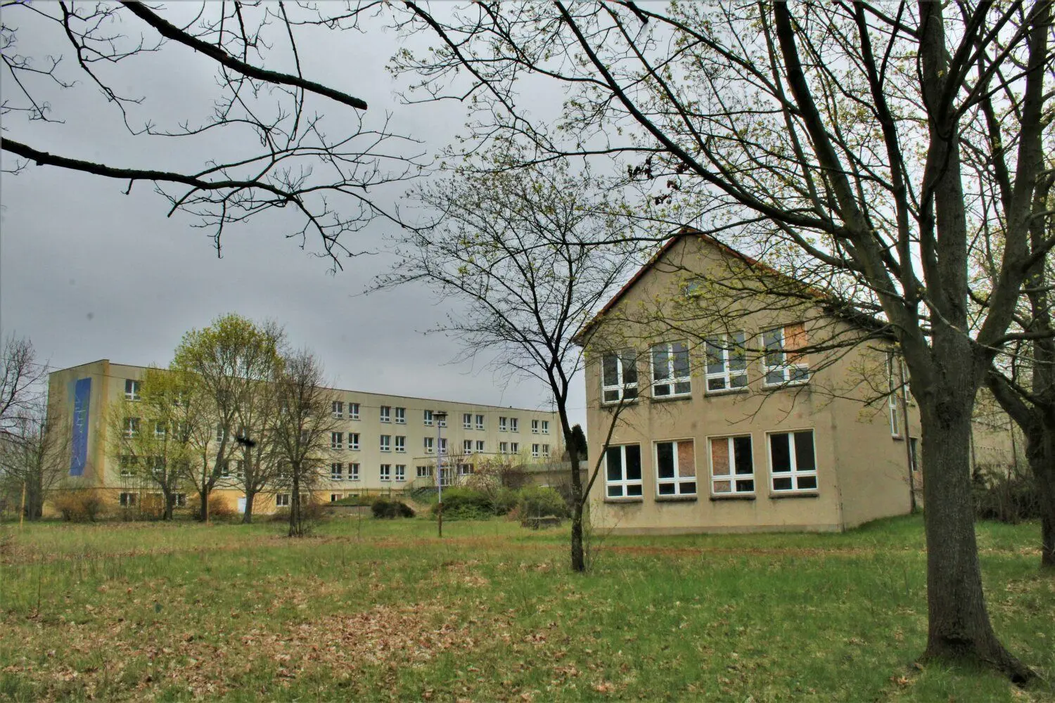 Im Hintergrund ist das einstige Schulgebäude zu erkennen, in dem bis 2013 Schüler unterrichtet wurden. Im Vordergrund ist eines der zwei Nebengebäude des Schulkomplexes in Groß Schacksdorf zu sehen.