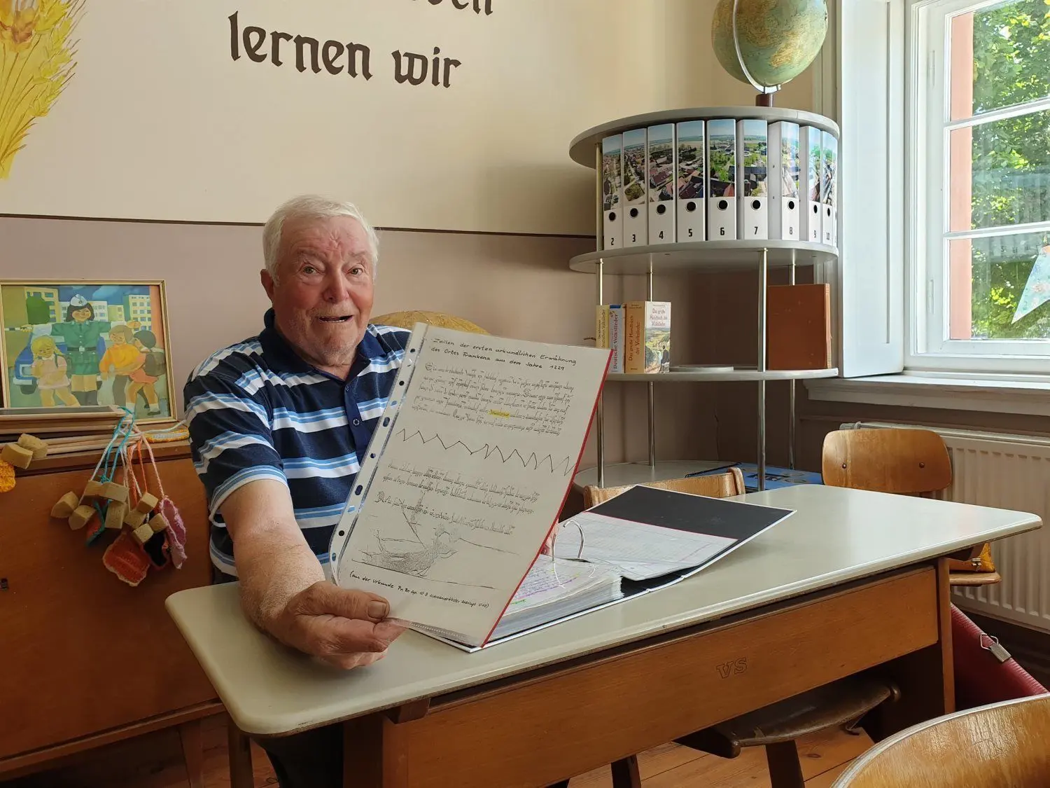 Horst Müller zeigt in der alten Schulstube die Urkunde über die Ersterwähnung von Frankena. Hinter ihm: 18 Ordner mit dem Luftbild-Fotomotiv seines Heimatdorfes, die er mittlerweile schon gefüllt hat. Bald kommt ein neues Kapitel aus der jüngeren Geschichte dazu.