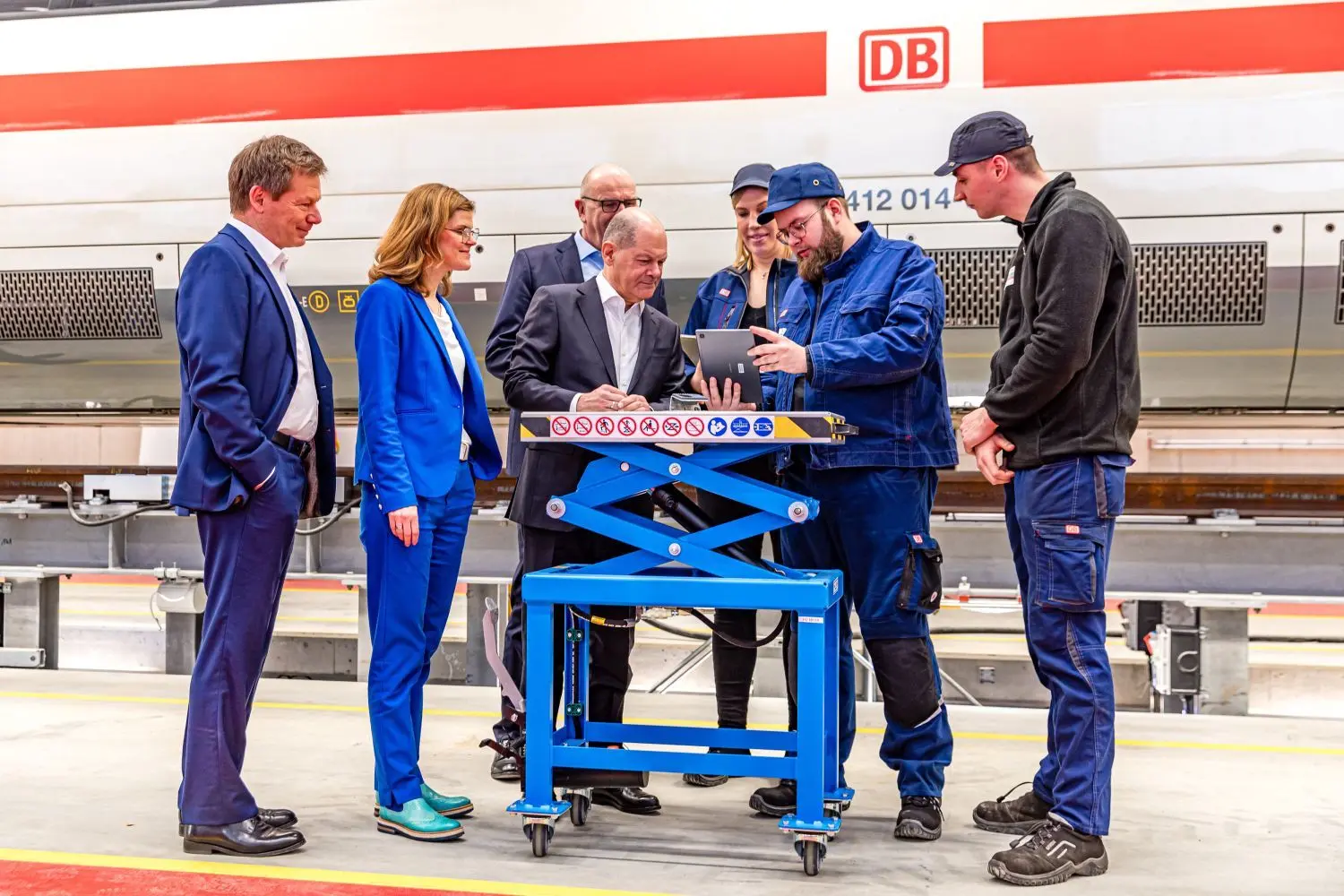 Die Bahnmitarbeiter Erik Hoffmann (von rechts), Tobias Saschowa und Hannah Weber demonstrieren Bundeskanzler Olaf Scholz (SPD), DB-Vorständin Daniela Gerd tom Markotten, Ministerpräsident Dietmar Woidke (SPD) und DB-Vorstandschef Richard Lutz wie mithilfe von Foto-Identifikation auf dem Tablet Bauteile bestellt werden können.