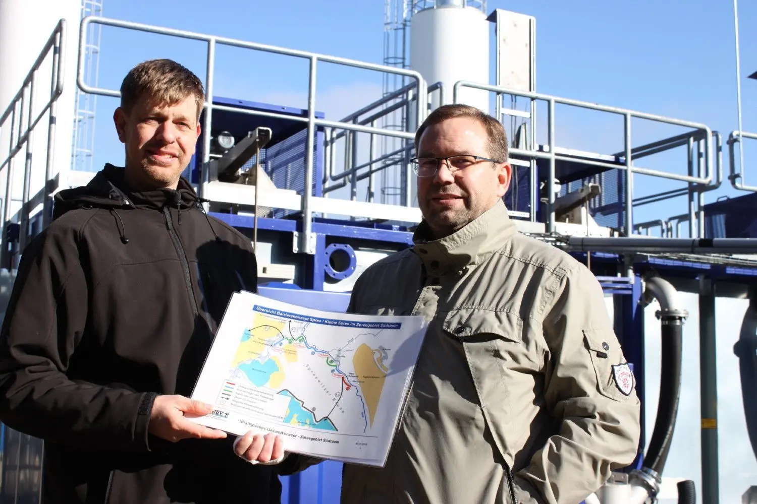 Neustadt/Spree: Sven Radigk und Marius Schlösser von der LMBV vor den Sedimentationscontainern der MWBA in Burgneudorf mit dem Barriekonzept, auf dem sämtliche Eisenminderungsmaßnahmen vermerkt sind.
