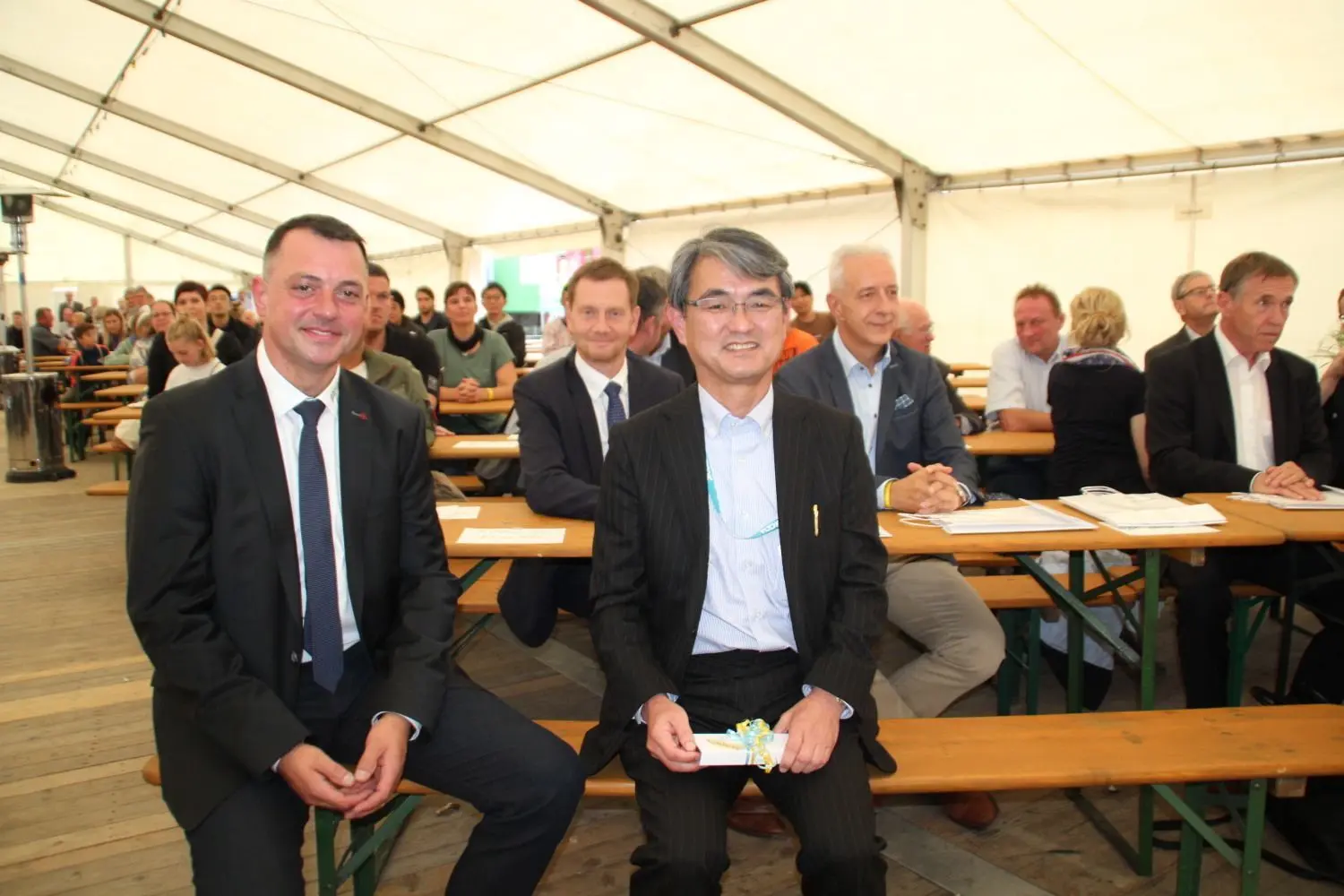 Eine gute Nachricht konnte TDDK-Geschäftsführer Kazushige Murao (vorn) am Rande des 20 Jahre-Firmenjubiläums in Straßgräbchen verkünden. Bei den Ehrengästen wie Ministerpräsident Michael Kretschmer (2.v.l.) und Vize-Landrat Udo Witschas (l.) sorgte das für große Freude.