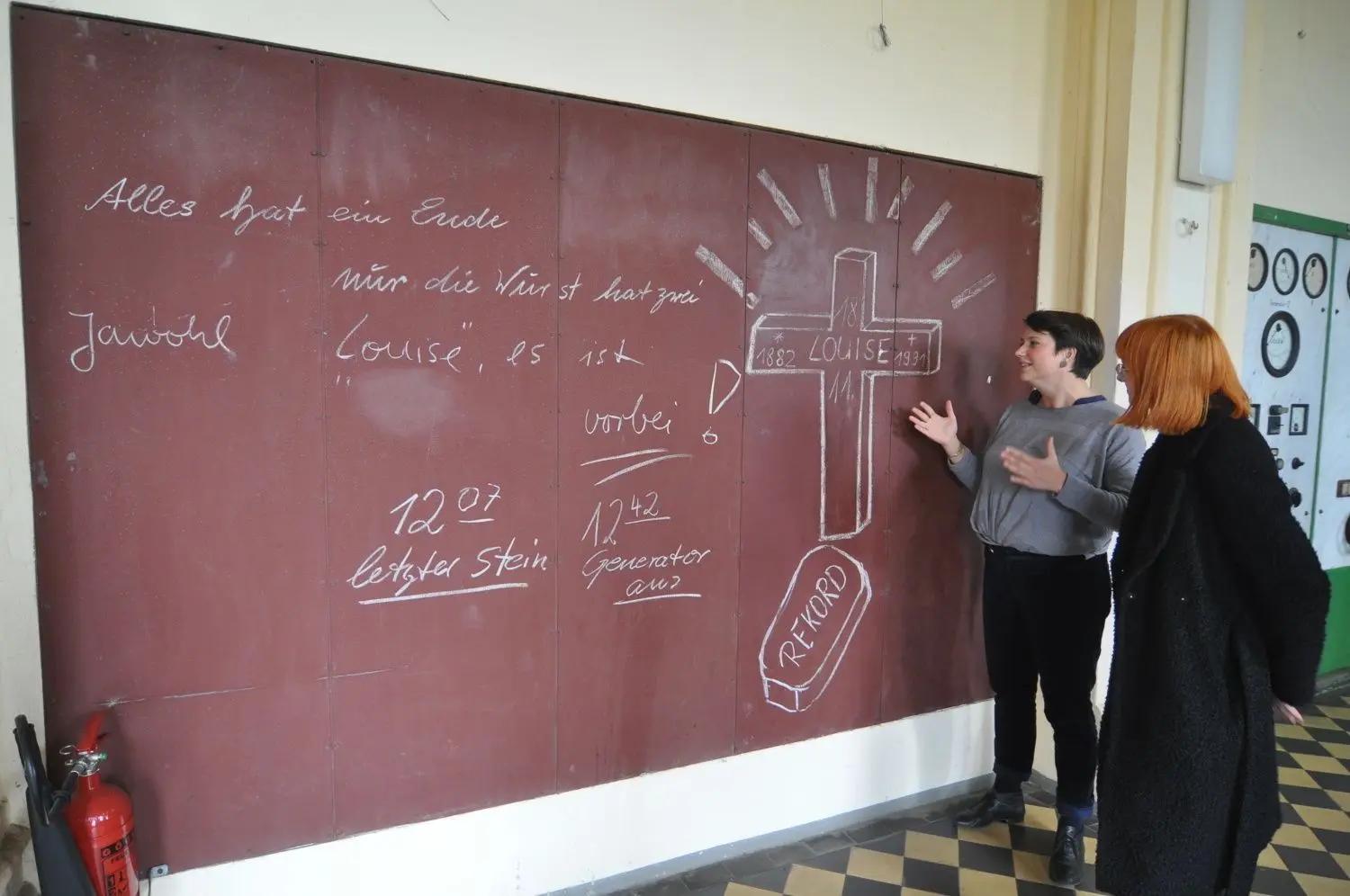 Vor 30 Jahren: Am 18. November 1991 wurde die Brikettfabrik Louise in Domsdorf stillgelegt. Museumsleiterin Kristin Rege (l.) zeigt Besuchern die mit Kreide beschriebene Tafel in der Maschinenhalle, die bis heute an das Ereignis erinnert.