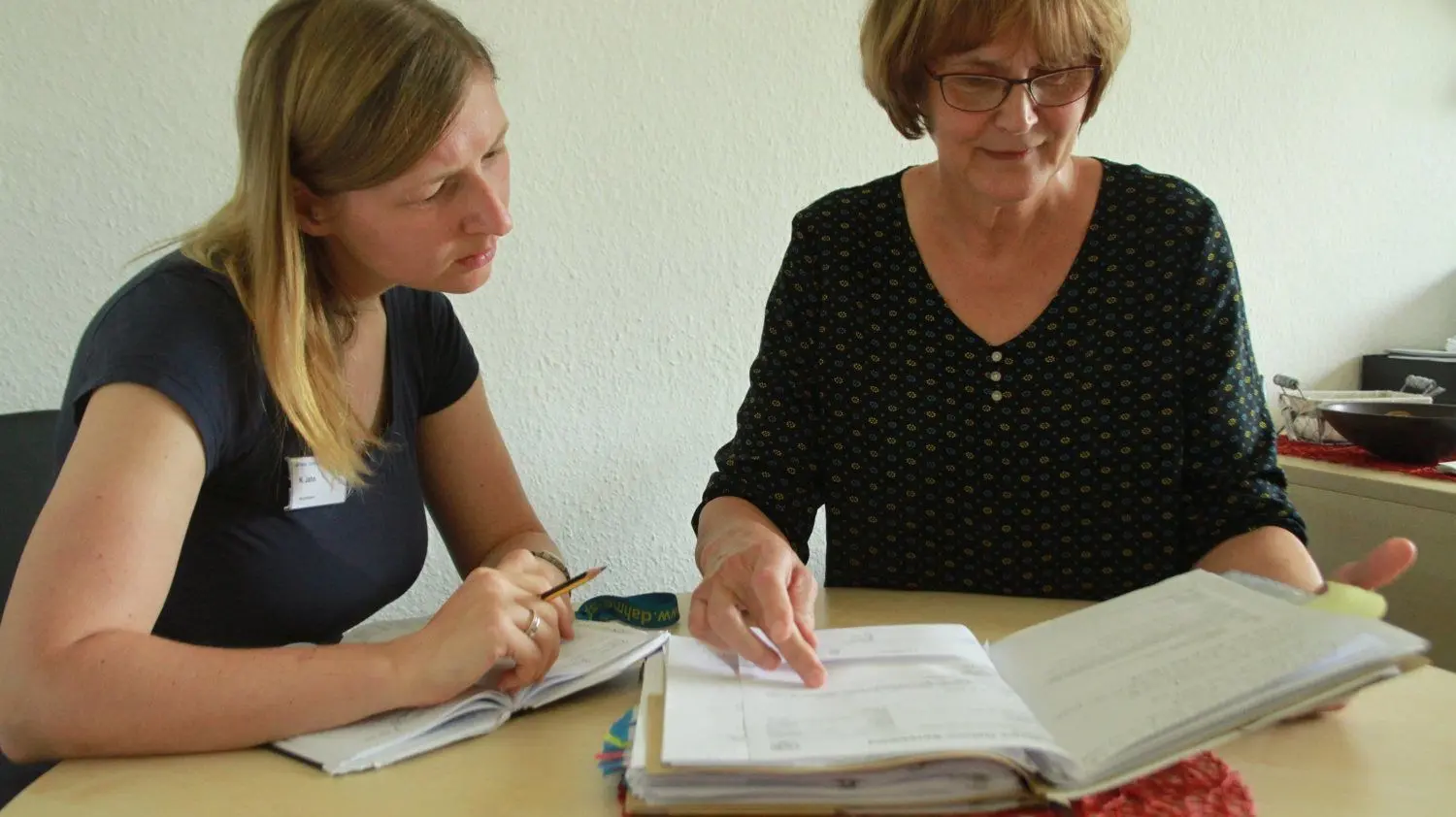 Nadine Jahn und Ruth Dubberke sitzen an ihrem Beratungstisch und schauen gemeinsam in einen Aktenordner. Sie beraten Menschen mit Behinderungen – und tauschen sich aus, wenn ihnen ein Fall besonders ans Herz geht.
