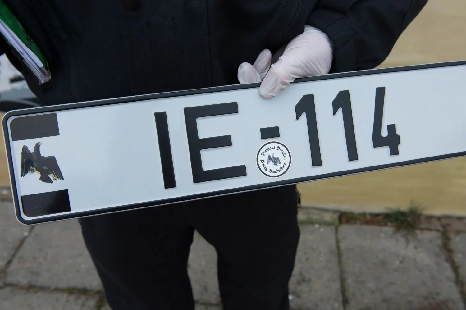 Ein Polizeibeamter hält ein illegales Autokennzeichen eines Reichsbürgers in der Hand.