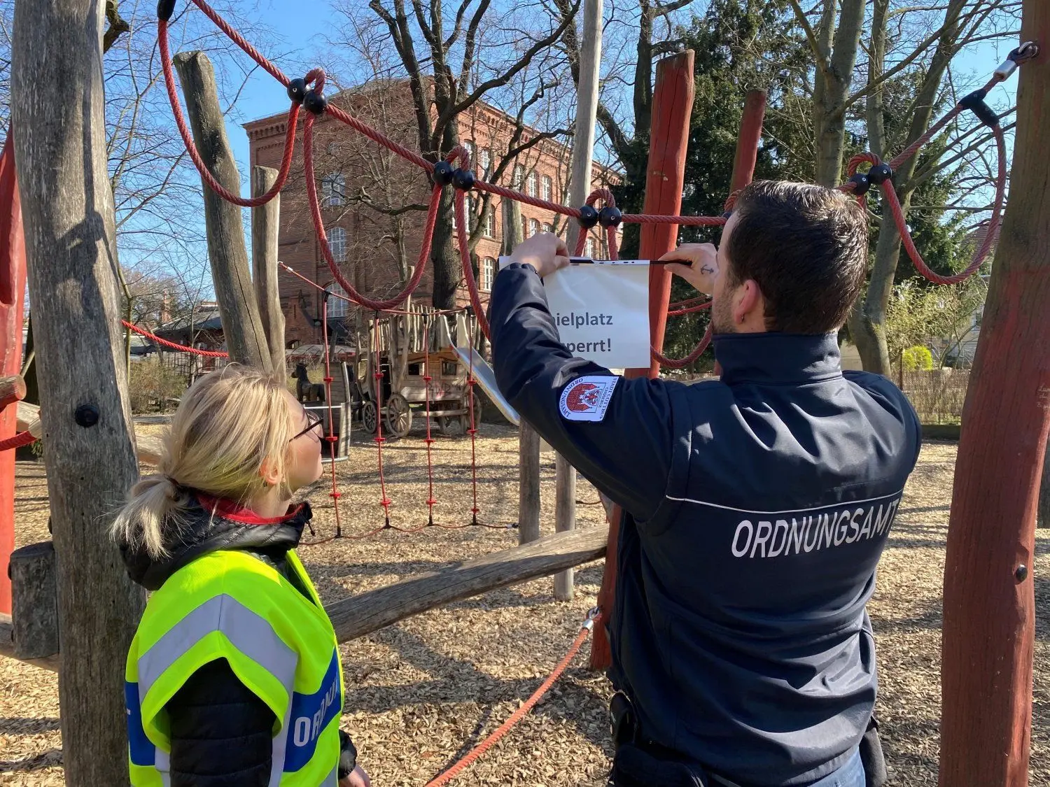 Ordnungsamt auf Streife:Tony Welzel und Michelle Marschall bringen im Puschkinpark ein Schild "Spielplatz gesperrt" an.