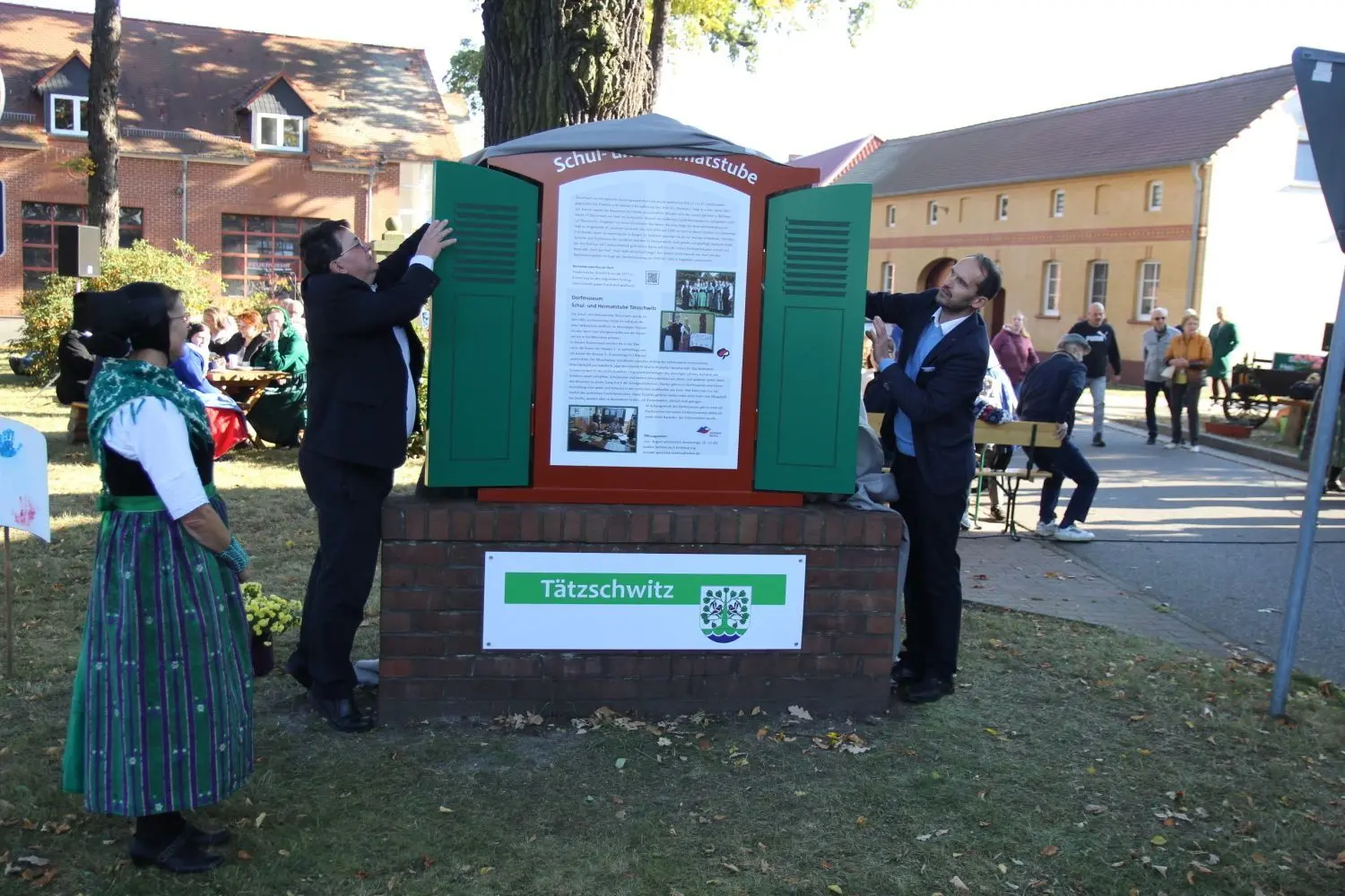 Der Elsterheider Bürgermeister Dietmar Koark und Maik Zschiesche (r.) vom Ortschaftsrat weihen im Beisein von Martina Petschick (l.) das neue Geschichtsfenster in der Tätzschwitzer Ortsmitte ein.