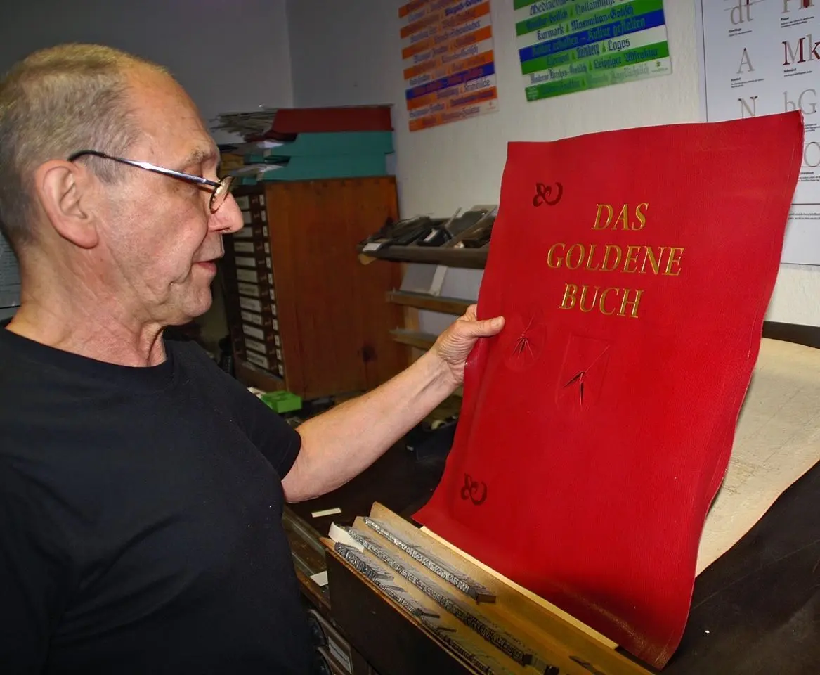 Buchbindermeister Reinhard Kußagk betrachtet die Goldprägung auf dem Buchdeckel. In die Aussparungen werden später die Medaillen eingelassen.