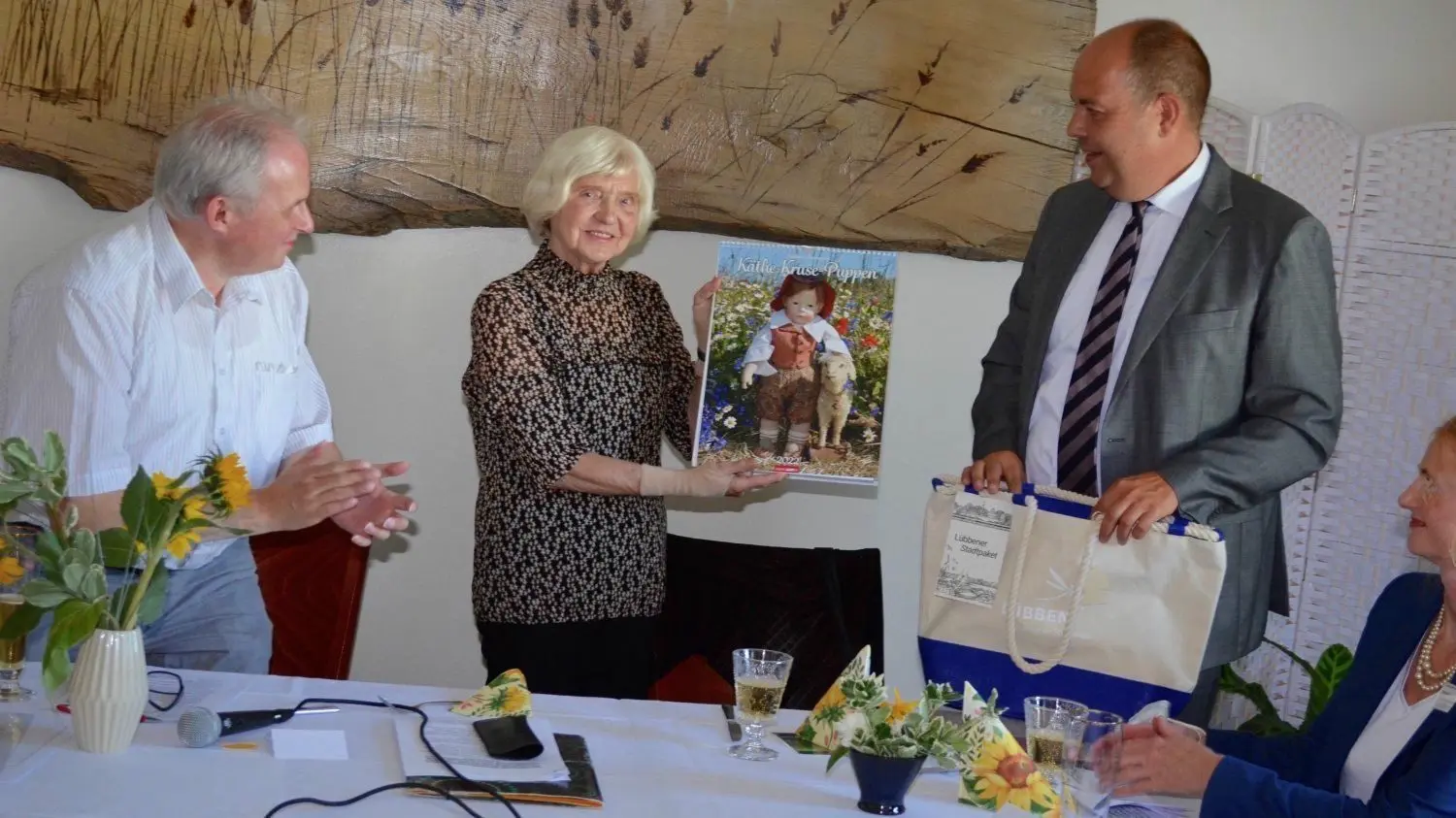 Lübbens Bürgermeister Lars Kolan (r.) hat Brigida Melzer (M.) einen Puppen-Kalender geschenkt. Der Vorsitzende Danilo Markewitz (l.) freut sich für die Ehrenvorsitzende.
