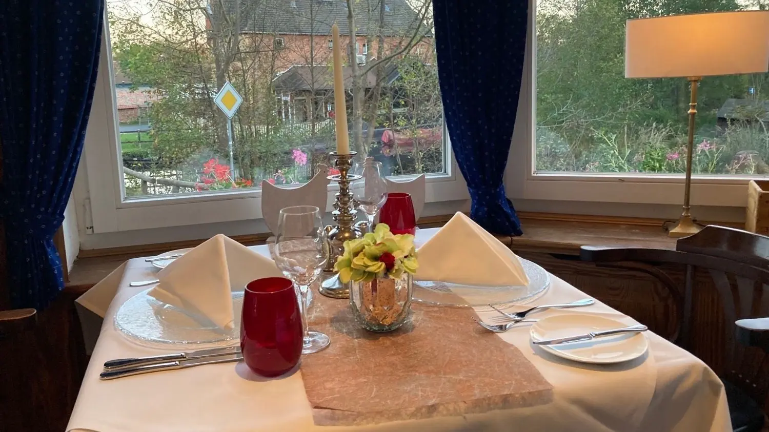 Alle Tische im Restaurant „Feine Küche - zum grünen Strand der Spree“ in Schlepzig sind am Fester platziert und mit gestärkten Leinentischtüchern, komplettem Menübesteck und Gläsern sowie frischen Blumen und Kerzen gedeckt.