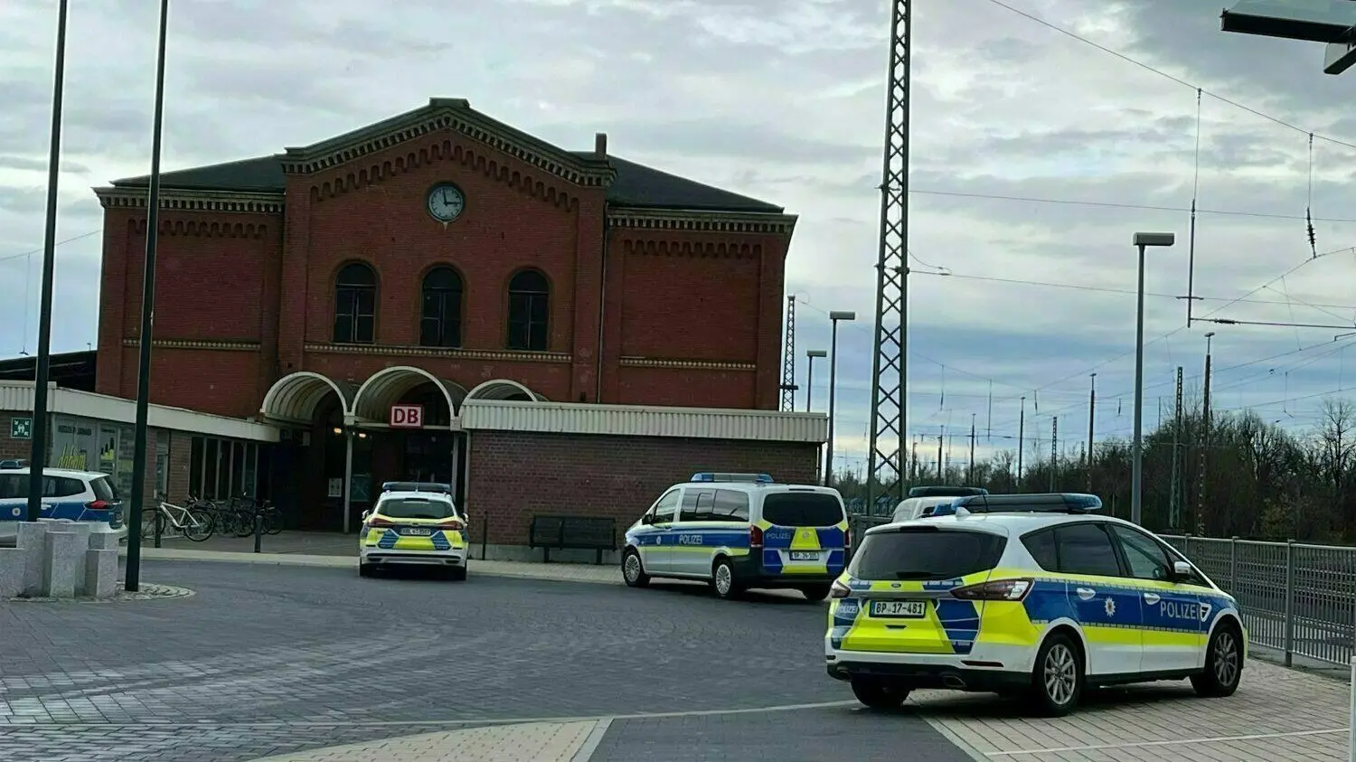 Polizeiautos stehen vor dem Bahnhof in Guben. Nachdem eine junge Frau in einem Zug mit einem „axtähnlichen Gegenstand“ angegriffen wurde, stoppte dort die Bahn.