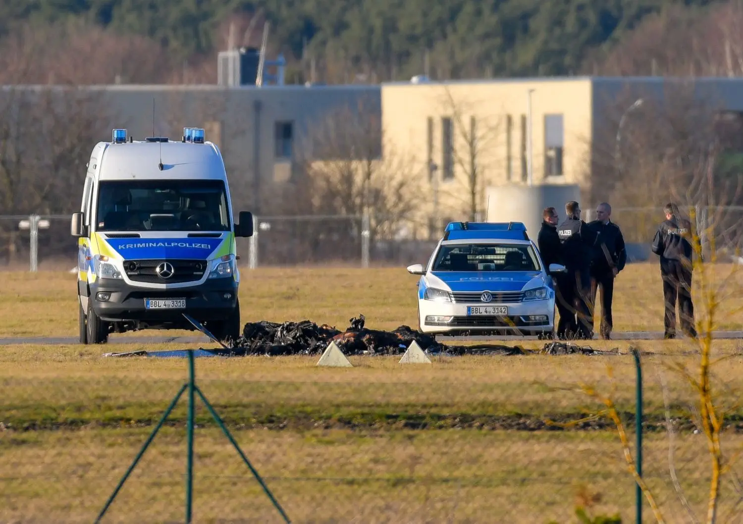 Zwischen zwei Fahrzeugen der Polizei sind die verkohlten Reste des abgestürzten Kleinflugzeuges auf dem Gelände des Flugplatzes Strausberg zu sehen.