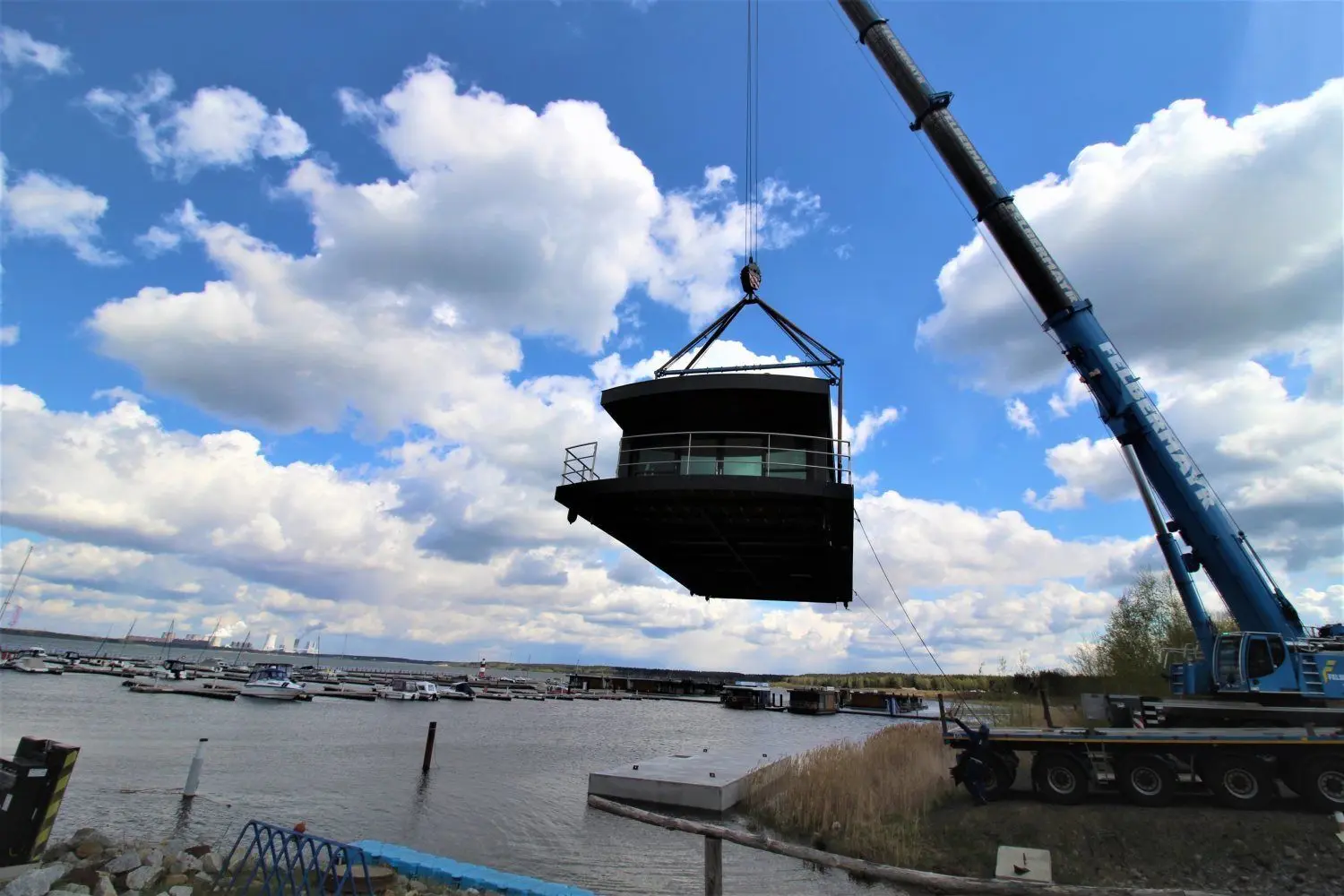 Mit dem Kran wird nunmehr das Haus auf den Ponton gesetzt. Im Hintergrund ist die Schwimmboot-Siedlung am Bärwalder See zu sehen.
