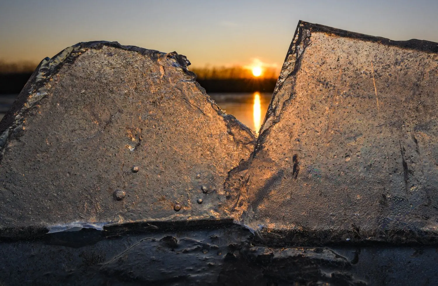 Kleine Eisstücken am Ufer des zugefrorenen Großen Storkower Sees schimmern im Gegenlicht des Sonnenuntergangs.