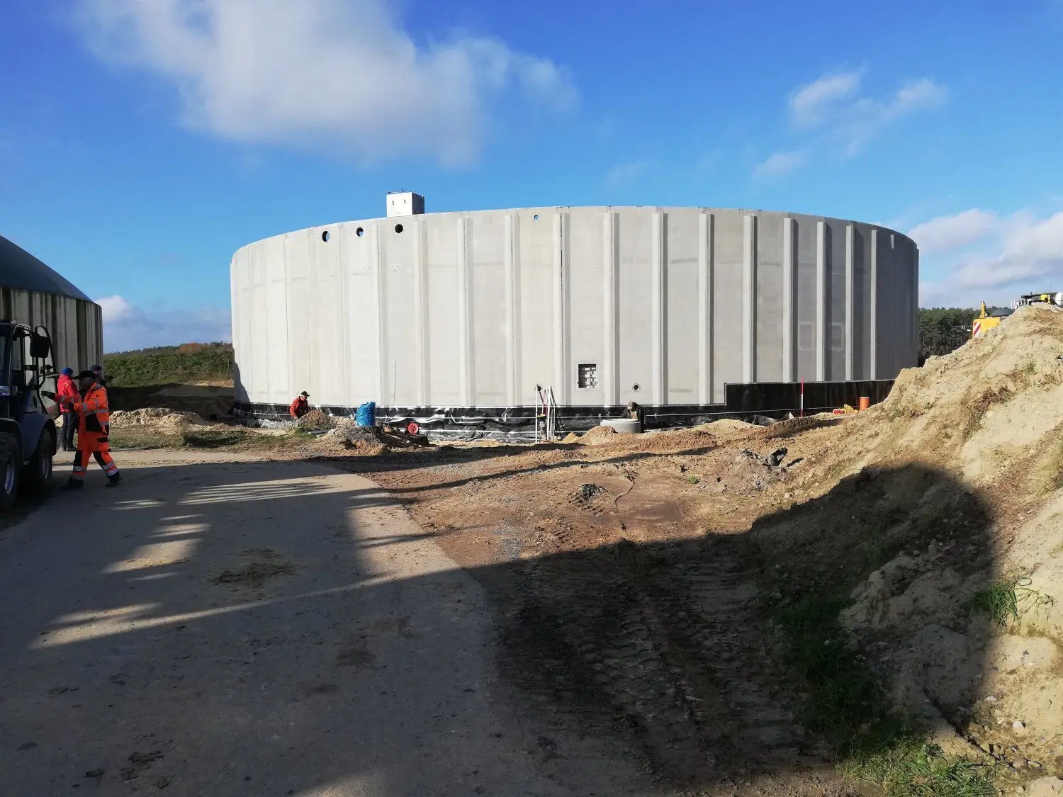 Hier entsteht ein neuer zusätzlicher Gärrestbehälter. Es wird der der größte der Biogasanlage Sembten. Der Bau ist von Vorteil für den angestrebten flexiblen Betrieb der Anlage. Der neue Speicher wird ebenso wie die bereits vorhandenen Gärrestbehälter, erkennbar an den grünen Kuppeln, auch als Gasspeicher gebraucht. Sie helfen, in Spitzenlastzeiten die Stromversorgung zu sichern. „Auch wenn unsere Blockheizkraftwerke das Biogas nicht mehr rund um die Uhr verstromen, sondern nur noch einige Stunden pro Tag, müssen wir weiterhin kontinuierlich das Biogas erzeugen und speichern, sodass genug Rohstoff da ist zum Verstromen in der Zeit des höchsten Strombedarfs“, erklärt Wilfried Pester.