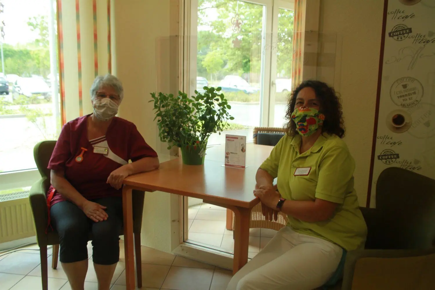 Elvira Kochan und Annett Bischoff sitzen mit Mund-Nasen-Schutz in einer der Nischen, die extra für sichere Besuche umgestaltet worden sind. Hinter der Glasscheibe sieht man einen Stuhl, auf dem Gäste Platz nehmen können - so sind die Bewohner geschützt, au