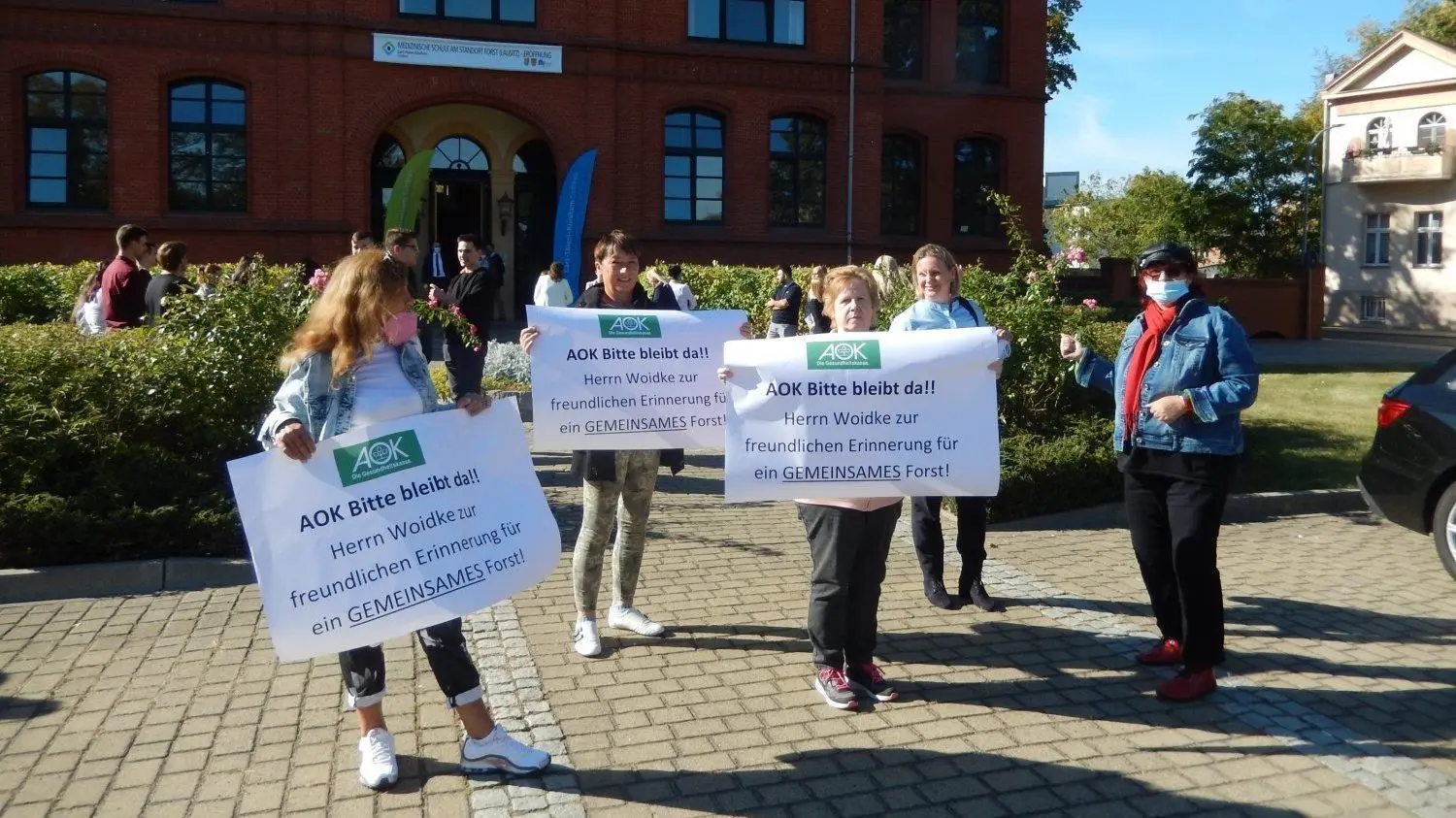 Bei Eröffnung der neuen Pflegschule in Forst mit Brandenburgs Ministerpräsidenten Dietmar Woidke (SPD) protestieren Forster Einwohner gegen die geplante Schließung der AOK-Geschäftsstelle im Ort.