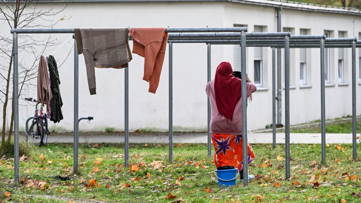 Wohnbaracken in der Erstaufnahmeeinrichtung der Zentralen Ausländerbehörde (ZABH) im Zossener Ortsteil Wünsdorf. Moderne Wohncontainer sind am Fuchsbau in Bad Saarow–Petersdorf geplant.
14.11.2023, Brandenburg, Zossen: Eine Frau hängt in der Erstaufnahmeeinrichtung der Zentralen Ausländerbehörde (ZABH) im Ortsteil Wünsdorf Wäsche auf. Mitglieder der Brandenburger Landesregierung besuchen Einrichtungen des Landkreises Teltow-Fläming. Foto: Jens Kalaene/dpa +++ dpa-Bildfunk +++