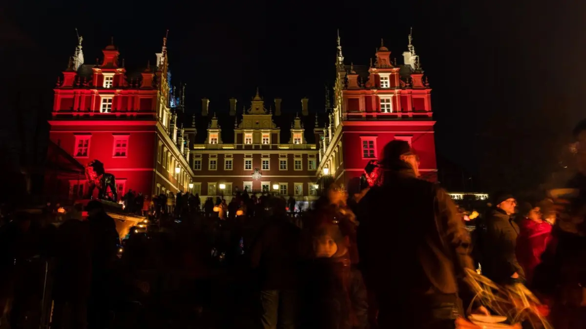 Besucher stehen beim Winterlichtfest 2023 auf der Wiese vor dem Neuen Schloss im Muskauer Park.
Besucher stehen auf der Wiese vor dem Neuen Schloss im Pückler Park. Beim Winterlichtfest wanderten nach zweijähriger Pause wieder mehr als 1000 Besucher von fünf verschiedenen Standorten im Park vom deutschen Bad Muskau und vom polnischen ??knica im Licht ihrer Lampions an farbig angestrahlten Bauten und Gehölzgruppen vorbei zum festlich angeleuchteten Neuen Schloss. Auf der Schlosswiese konnten sich die Wanderer stärken und Swingmusik live hören und sehen.