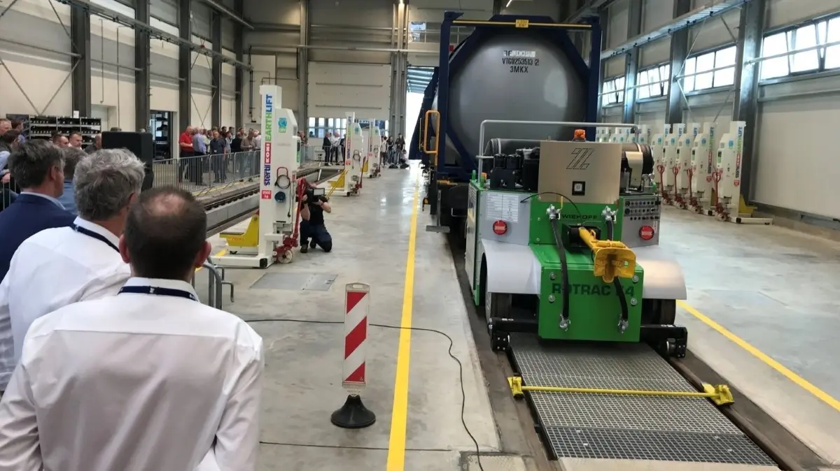 Die ersten zwei Waggons rollen in die neue Instandsetzungshalle des VTG Güterwagenzentrums Lausitz.
Wagons in einer Halle, Menschen, Eröffnung von VTG