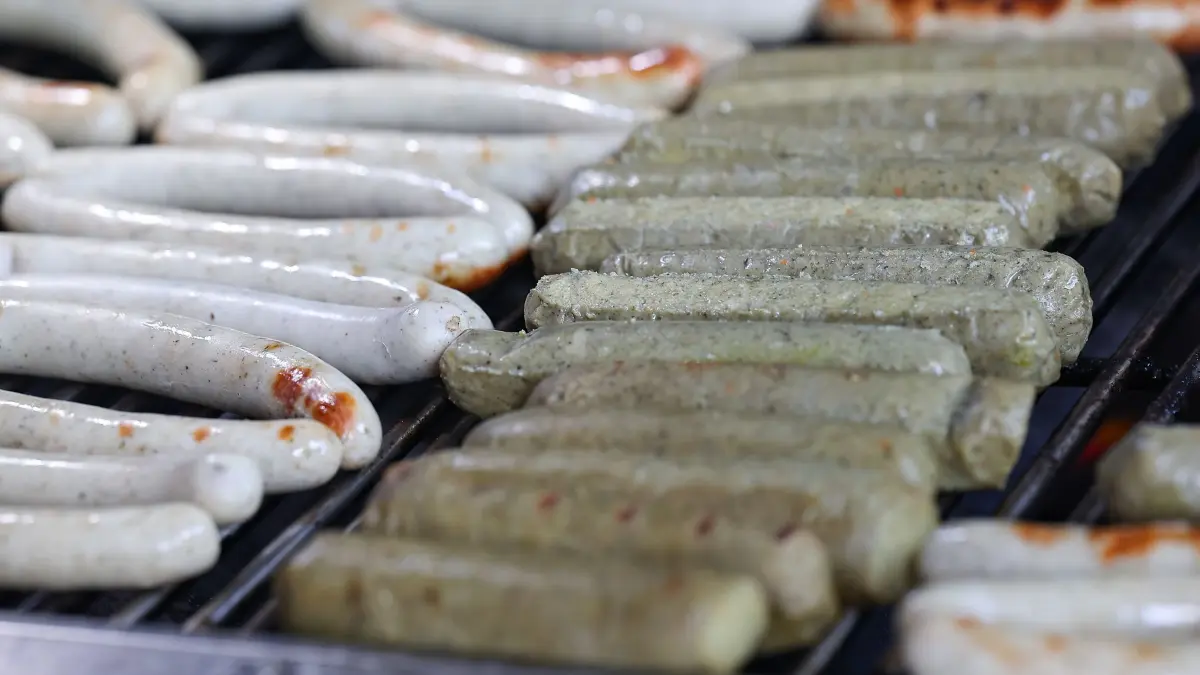 Fränkischer Bratwurstgipfel: 12.05.2024, Bayern, Pegnitz: Echte Bratwürste (l) und vegane Bratwürste (r) liegen nebeneinander auf dem Holzkohlengrill. Zehn Metzgereien aus Franken kämpfen beim Fränkischen Bratwurstgipfel um den Titel der Fränkischen Bratwurstkönigin oder des Fränkischen Bratwurstkönigs. (zu dpa: «Ein «Versucherla» vom Kulturgut: In Franken steigt der Bratwurstgipfel») Foto: Daniel Löb/dpa +++ dpa-Bildfunk +++