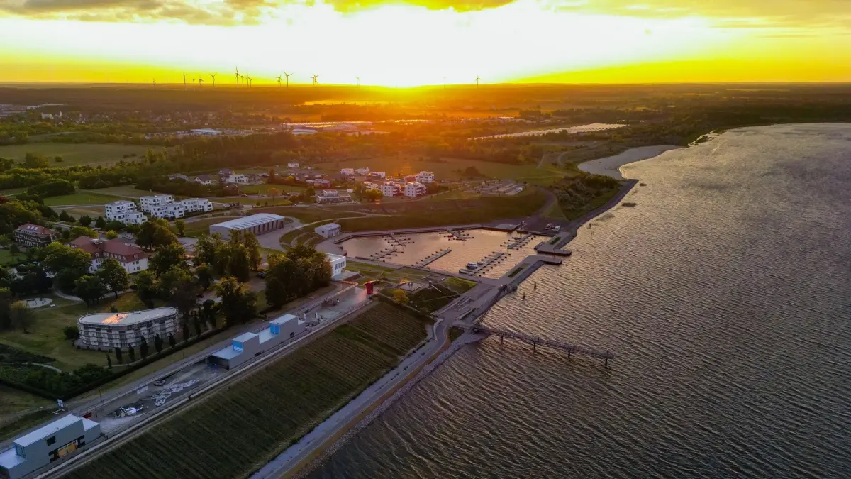 Start für den Großräschener See: 17.05.2024, Brandenburg, Großräschen: Der Großräschener See mit seinem Hafen am frühen Morgen kurz nach dem Sonnenaufgang (Luftaufnahme mit einer Drohne). Nach Auskunft der Lausitzer und Mitteldeutsche Bergbau-Verwaltungsgesellschaft mbH (LMBV) soll ab Pfingsten der Großräschener See für eine definierte Anzahl von Booten und Wasserfahrzeugen für die Saison 2024 frei gegeben werden. Der für eine Zwischennutzung notwendige Mindestwasserstand im Bergbaufolgesee wurde zum Beginn der Saison erreicht. Der Hafen Großräschen wurde bereits im Jahr 2019 eröffnet. Mit der Futung des ehemaligen Braunkohletagebaus wurde im Jahr 2007 begonnen. Für 2026 wird angestrebt, dass die Restlochkette - mit dem Sedlitzer See, dem Geierswalder See und dem Partwitzer See - zusammen mit dem Großräschener See in die dauerhafte Nutzung gehen könnte. Foto: Patrick Pleul/dpa/ZB - Honorarfrei nur für Bezieher des Dienstes ZB-Funkregio Ost +++ ZB-FUNKREGIO OST +++