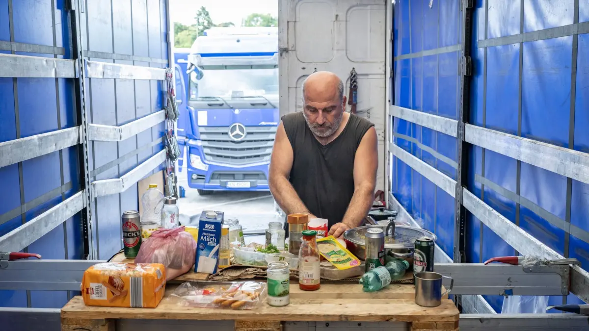Lkw–Streik auf Rastplatz in Hessen: ARCHIV - 19.07.2023, Hessen, Gräfenhausen: Lastwagenfahrer Zurab aus Georgien bereitet sich auf der Ladefläche seines LKW Abendessen zu. Gemeinsam mit anderen Fahrern einer polnischen Spedition ist er auf dem Rastplatz Gräfenhausen an der A5 in Hessen in Streik getreten, um ausstehende Löhne einzufordern. Foto: Boris Roessler/dpa +++ dpa-Bildfunk +++