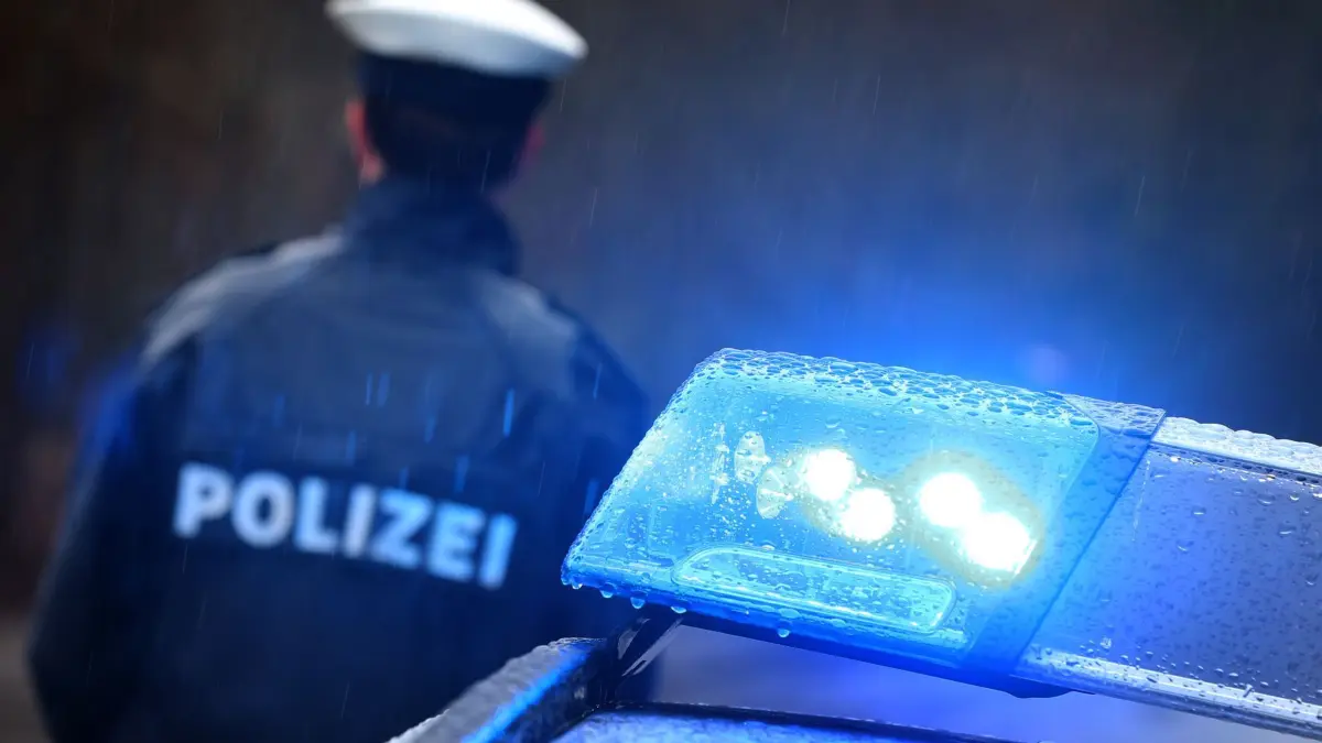Symbolbild: ARCHIV - 15.03.2019, Bayern, Kempten: ILLUSTRATION - Ein Polizist steht im Regen vor einem Streifenwagen dessen Blaulicht aktiviert ist. Eine junge Frau soll einen vier Jahre alten Bub in Eschenbach in der Oberpfalz mit Gewalt getötet haben. Sie sitze wegen des Verdachts des Totschlags in Untersuchungshaft, teilte die Polizei am Freitag mit. (zu dpa: «Immer mehr Gewalt gegen Polizisten») Foto: Karl-Josef Hildenbrand/dpa +++ dpa-Bildfunk +++