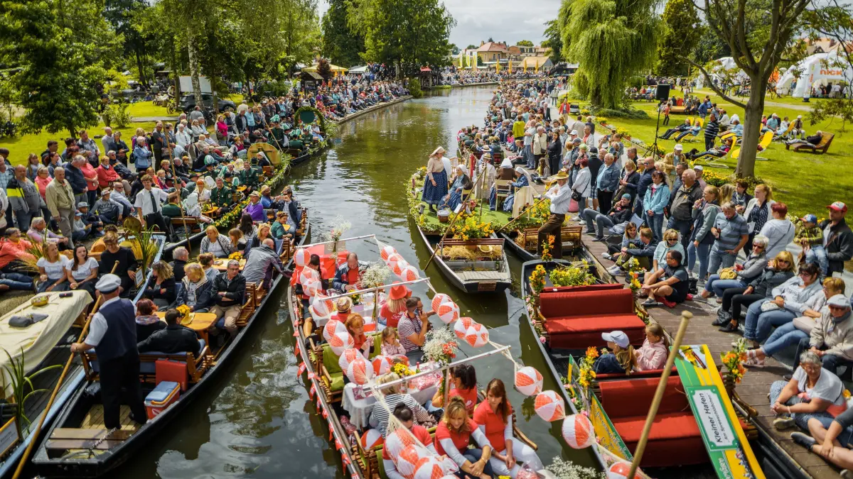 Viele Menschen versammeln sich zum Kahnkorso im Spreewald. Die Stadtkapelle fährt vorne weg, gefolgt von Kähnen, die die spreewälder Lebensweisen und Traditionen repräsentieren.