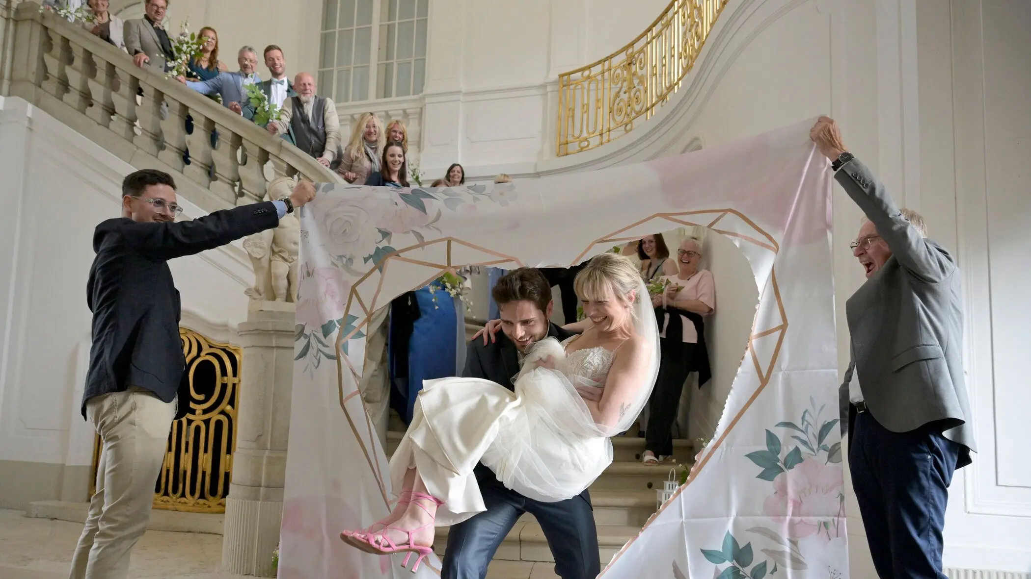 Unter den Augen ihrer Familien trägt Toni aus Lübben (2. von links) seine Braut Pia (rechts daneben) durch ein Herz, dass die beiden zuvor aus einem Bettlaken ausschneiden mussten. Wird er sie auch weiter auf Händen tragen?