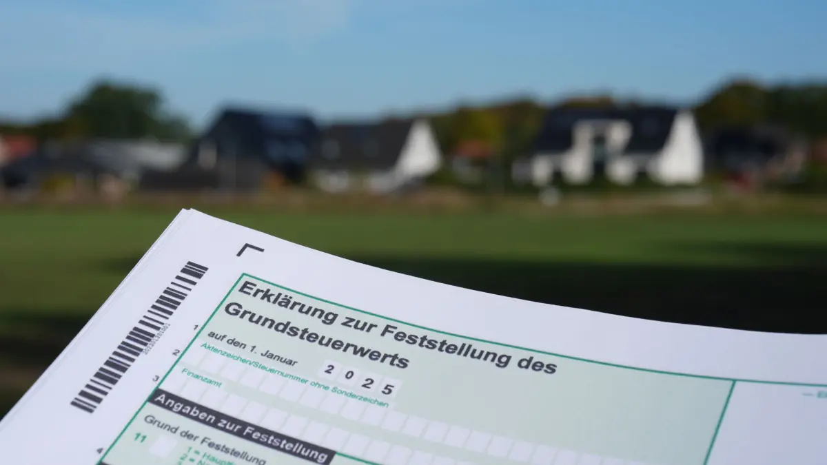 Ein Erklärung zur Feststellung des Grundsteuerwerts für das Jahr 2025 wird vor eine Wohnsiedlung hochgehalten. (zu dpa: «Was verbirgt sich hinter der Grundsteuer und der Reform?») +++ dpa-Bildfunk +++