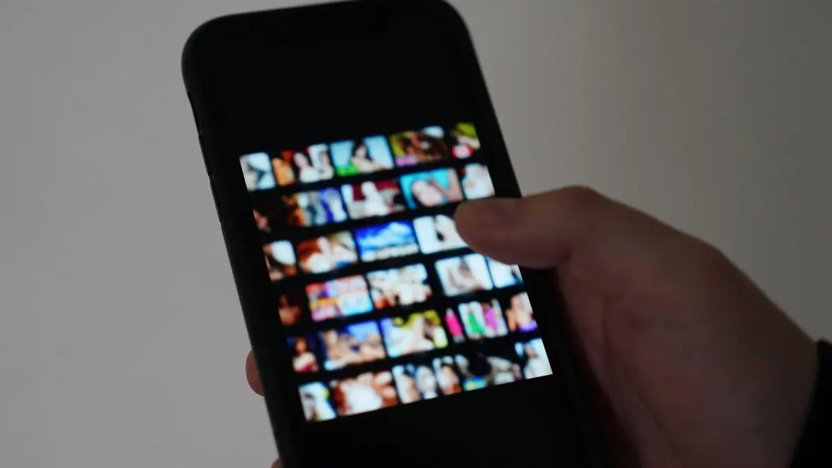 Mann schaut sich Nacktbilder auf dem Smartphone an: ILLUSTRATION - «Sextortion» beginnt mit einem vermeintlichen Online-Flirt und endet mit der Drohung, intime Bilder oder Videos zu veröffentlichen. (zu dpa: «Erpressung mit intimen Fotos: So schützen Eltern ihre Kinder») Foto: Marcus Brandt/dpa/dpa-tmn - Honorarfrei nur für Bezieher des dpa-Themendienstes +++ dpa-Themendienst +++