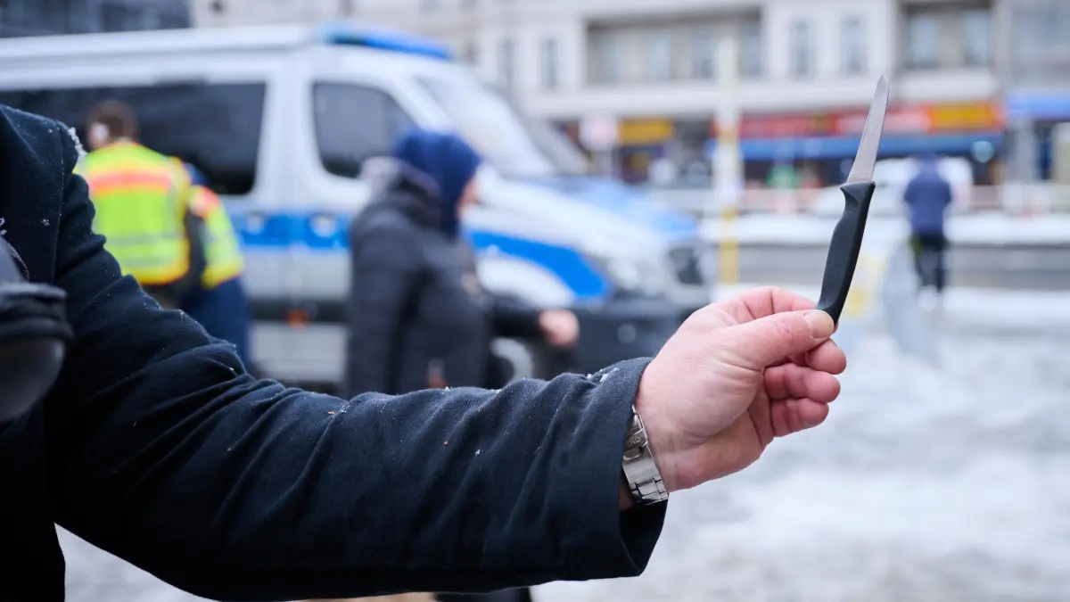 Eine Person hält ein Küchenmesser in der Hand, das an einem Marktstand verkauft wird, während Polizeibeamte Flyer in unterschiedlichen Sprachen verteilen und Menschen auf dem Leopoldplatz in Berlin-Wedding über das neue Gesetz aufklären.