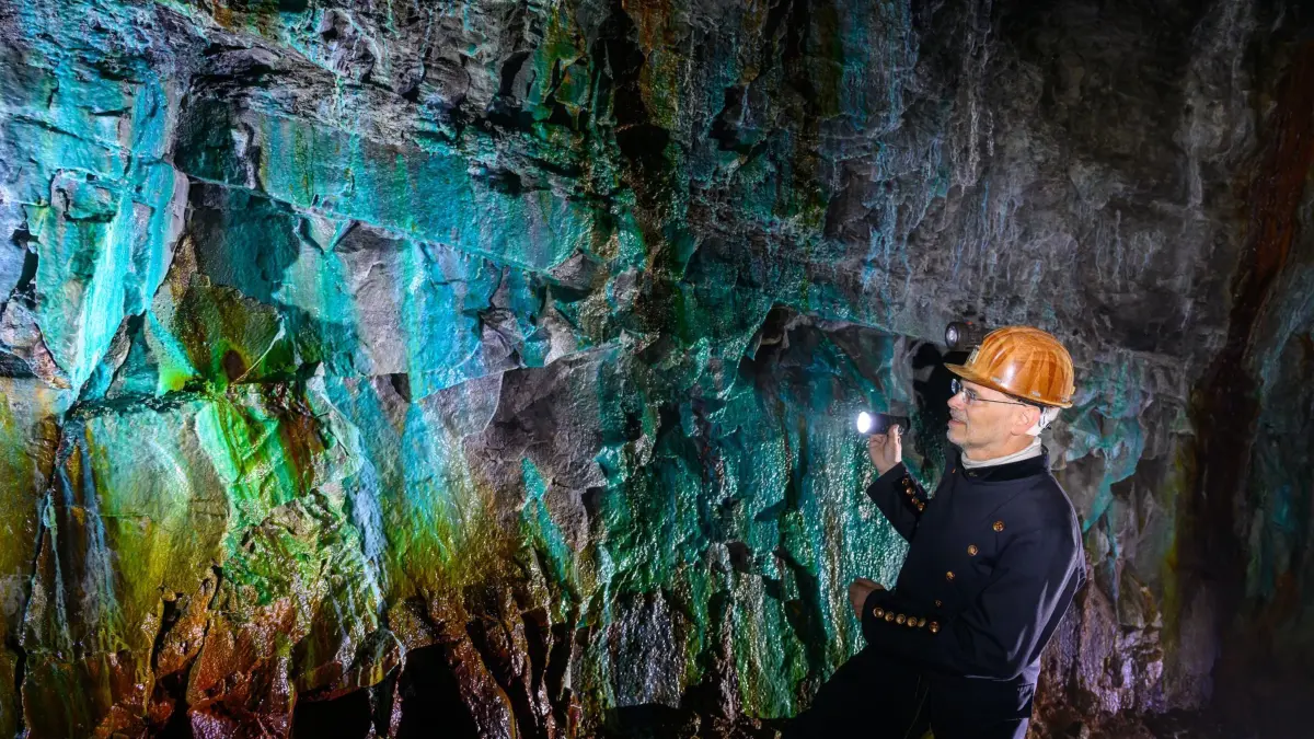 825 Jahre Kupferbergbau im Mansfelder Land: PRODUKTION - 02.04.2025, Sachsen-Anhalt, Sangerhausen: In fast 300 Metern Tiefe steht Thomas Wäsche, Leiter des "ErlebnisZentrum Bergbau Röhrigschacht Wettelrode", unter Tage im sogenannten Grünen Gewölbe. Die Versinterungen sind durch gelöste Mineralien aus dem Kalkgestein entstanden. Die Farbpalette reicht von kräftigen Brauntönen über Weiß, Grün, Türkis, Blau bis Schwarz. Die ersten Bergleute begannen im Mansfelder Land vor 825 Jahren nach Kupfererz zu graben. Ab dem Jahr 1750 wurde intensiv Bergbau betrieben. Insgesamt wurden aus dem Erz des Gebietes rund 2,6 Millionen Tonnen Kupfer und 14.213 Tonnen Silber gewonnen. Mit insgesamt 38 Veranstaltungen wird bis Dezember an den Beginn des Bergbaus und der Verhüttung in der Region des Mansfelder Landes erinnert. Als großer Kupfer- und Silberproduzent trug die Region über Jahrhunderte hinweg zur wirtschaftlichen Entwicklung bei. (zu dpa: «Mansfelder Land feiert 825 Jahre Kupferbergbau») Foto: Hendrik Schmidt/dpa +++ dpa-Bildfunk +++