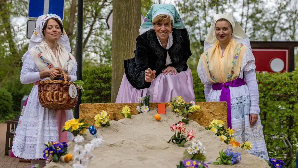 Osterfest mit Spreewälder Traditionen: 19.04.2025, Brandenburg, Lübben: Doris Strasen (M), lässt, beobachtet von Vivien Fiebig (l) und Antonia Lanto, Erzieherinnen in der Kita Spreewald, ein Ei über den Parcous beim sogenannten Waleien rollen. Hier geht es darum, mit seinem Ei ein bereits auf dem Parcours liegendes fremdes Ei zu treffen. Gelingt dies, darf man das fremde Ei mitnehmen. Gelingt es nicht, bleibt das eigene Ei mit den anderen liegen. Doris Strasen hat vor 30 Jahren, damals selbst Erzieherin der Kita Spreewald, die alte Tradition des Waleiens, wiederbelebt und feiert in diesem Jahr das Jubiläum mit ihren Nachfolgerinnen und allen Besucheren beim Osterfest auf der Schlossinsel. Foto: Frank Hammerschmidt/dpa +++ dpa-Bildfunk +++