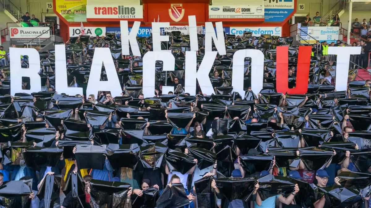 Betriebsversammlung mit Protest beim Unternehmen Leag: 12.06.2025, Brandenburg, Cottbus: Mitarbeiter der Lausitz Energie Bergbau AG (Leag) halten während einer Betriebsversammlung im Cottbuser Stadion den Spruch «Kein Blackout» hoch. Beschäftigte des Energiekonzerns Leag befürchten beim Bau neuer Gaskraftwerke im Nachteil gegenüber dem Süden Deutschlands zu sein. Nach eigenen Angaben sind zur Betriebsversammlung im Stadion in Cottbus etwa 1.500 Mitarbeiter erschienen. Aussagen von Bundeswirtschaftsministerin Katherina Reiche (CDU) zu einem «Südbonus» bei neuen Gaskraftwerken lösen Sorgen bei der Leag in der Lausitz aus. Foto: Patrick Pleul/dpa +++ dpa-Bildfunk +++