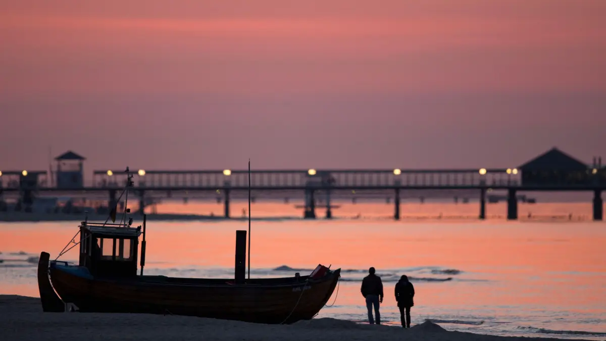 dpatopbilder Urlauber gehen am 29.04.2014 vor der Seebrücke des Ostseebades Heringsdorf (Mecklenburg-Vorpommern) auf der Insel Usedom vor dem von der untergehenden Sonne verfärbten Himmel am Strand spazieren. Die zweitgrößte deutsche Insel wird im Jahr von rund 1,6 Millionen Touristen besucht. Foto: Jens Büttner/dpa ++ +++ dpa-Bildfunk +++