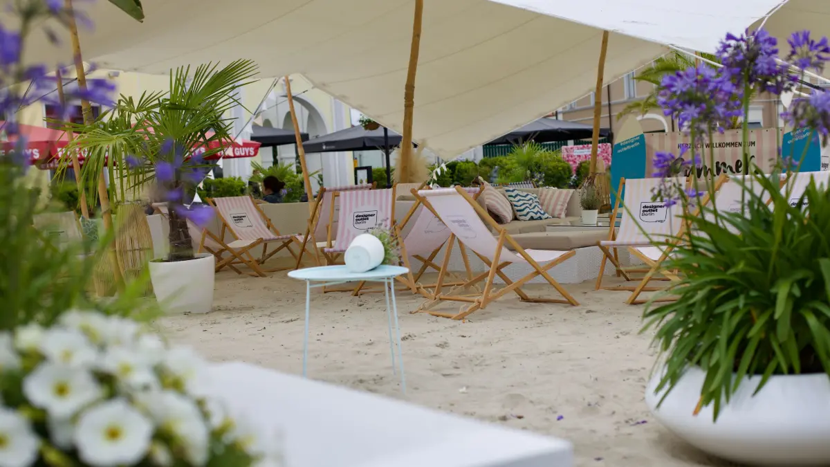 Strand im Designer-Outlet Wustermark: Palmen, Liegestühle und Sonnenschirme sollen Urlaubsgefühle wecken. Für die Kinder steht Sandspielzeug bereit.