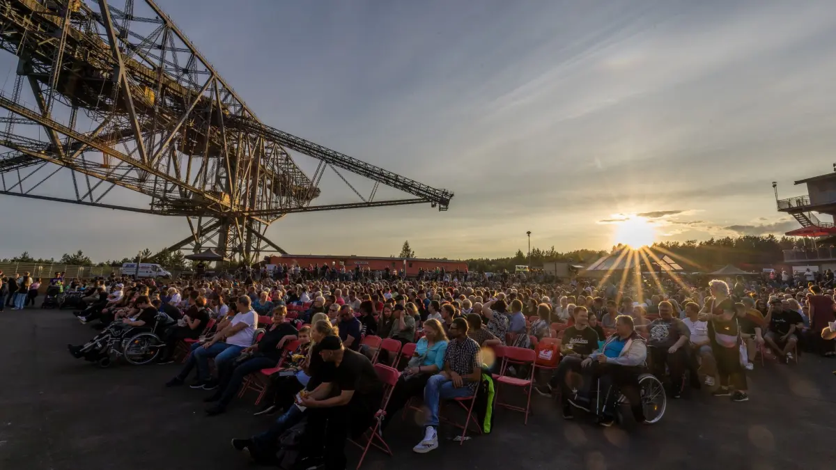 Pyro Games - Duell der Feuerwerker: 02.08.2025, Brandenburg, Lichterfeld-Schacksdorf: Besucher der Pyro Games versammeln sich unter der Förderbrücke F60 am Besucherbergwerk Lichterfeld und warten hier bei einem Bühnenprogramm auf Dunkelheit und den Beginn der Feuerwerksveranstaltung. Der Auftakt der Pyro Games findet regelmäßig vor der beeindruckenden Kulisse des Besucherbergwerkes F60 statt. Sie sind ein Feuerwerksfestival, bei dem drei Pyrotechnik-Teams in einem Wettbewerb mit Musik synchronisierte Feuerwerke präsentieren. Begleitet wird die Veranstaltung von einem Rahmenprogramm mit Live-Musik und diversen Shows. Foto: Frank Hammerschmidt/dpa +++ dpa-Bildfunk +++