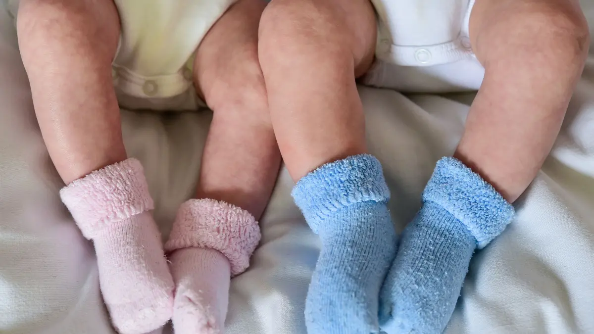 ILLUSTRATION - Rosa und blaue Söckchen für ein Mädchen und einen Jungen und die nackten Babybeine von Zwillingen, aufgenommen in einem Babybettchen. Weltweit werden einer Studie zufolge mehr Zwillinge geboren als je zuvor. (zu dpa: «Studie: Zahl der Zwillingsgeburten weltweit auf Rekordstand») +++ dpa-Bildfunk +++