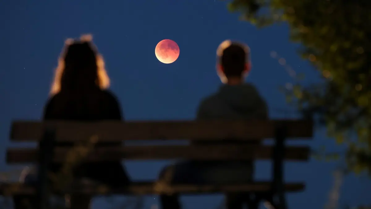 Totale Mondfinsternis - Leipzig: 07.09.2025, Sachsen, Leipzig: Schaulustige betrachten von einer Parkbank aus die auch als Blutmond bezeichnete totale Mondfinsternis. Dabei schiebt sich der Mond nach und nach in den Erdschatten schieben - bis hin zur totalen Mondfinsternis. Foto: Jan Woitas/dpa +++ dpa-Bildfunk +++